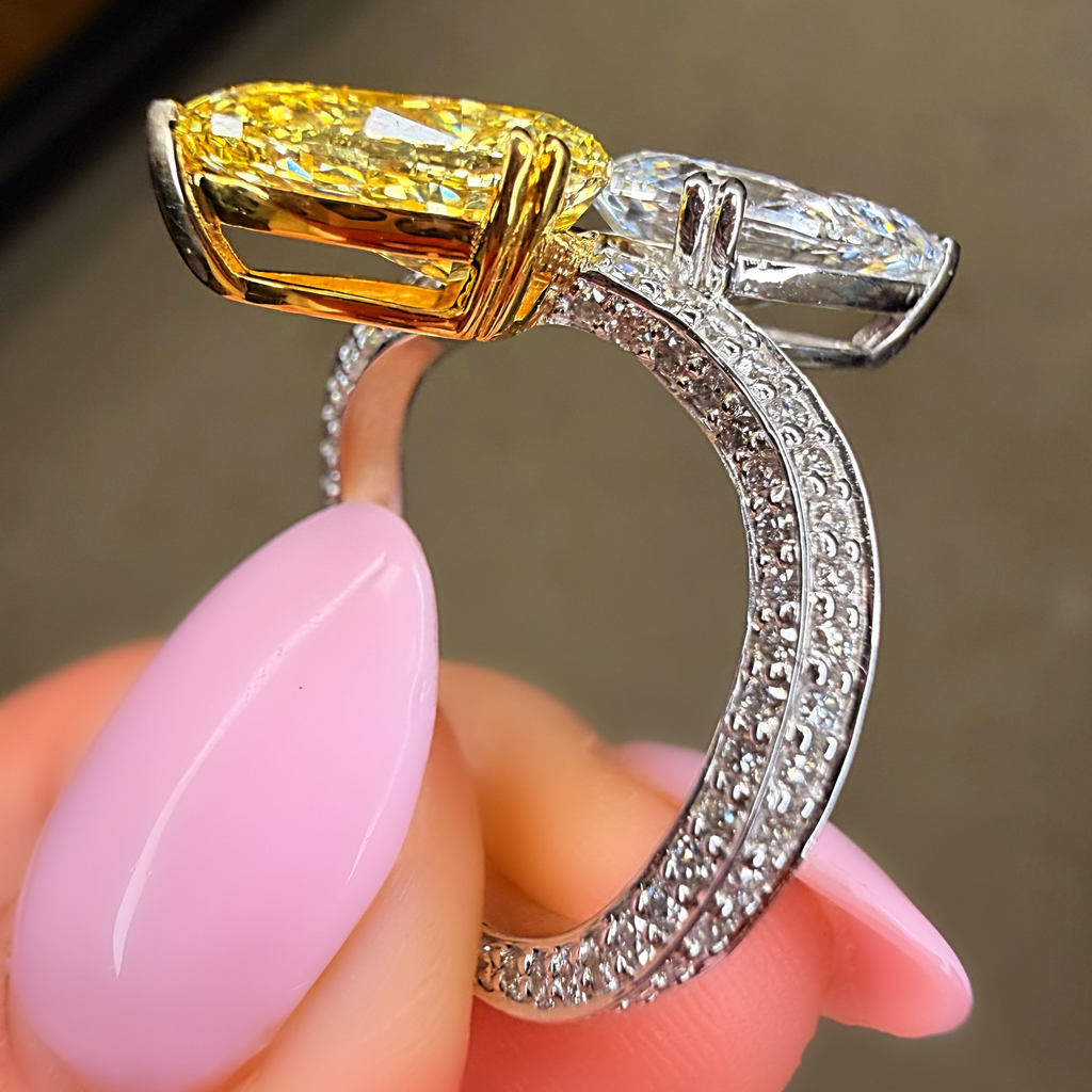 Gold and silver ring with a large yellow gemstone held by a hand with pink nail polish.
