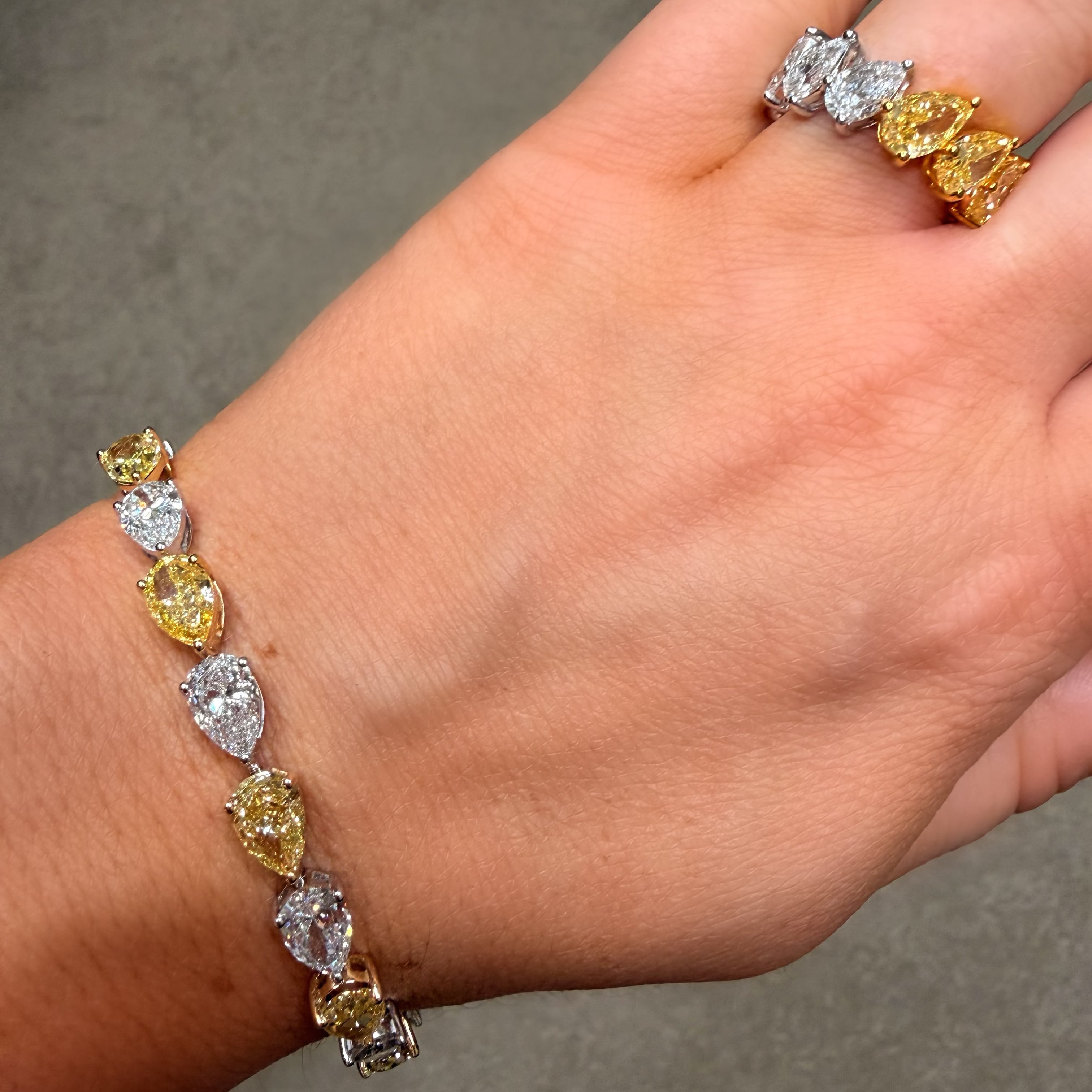 WOMANS HAND WEARING A YELLOW AND WHITE DIAMOND PEAR TENNIS BRACELET AND MATCHING RING