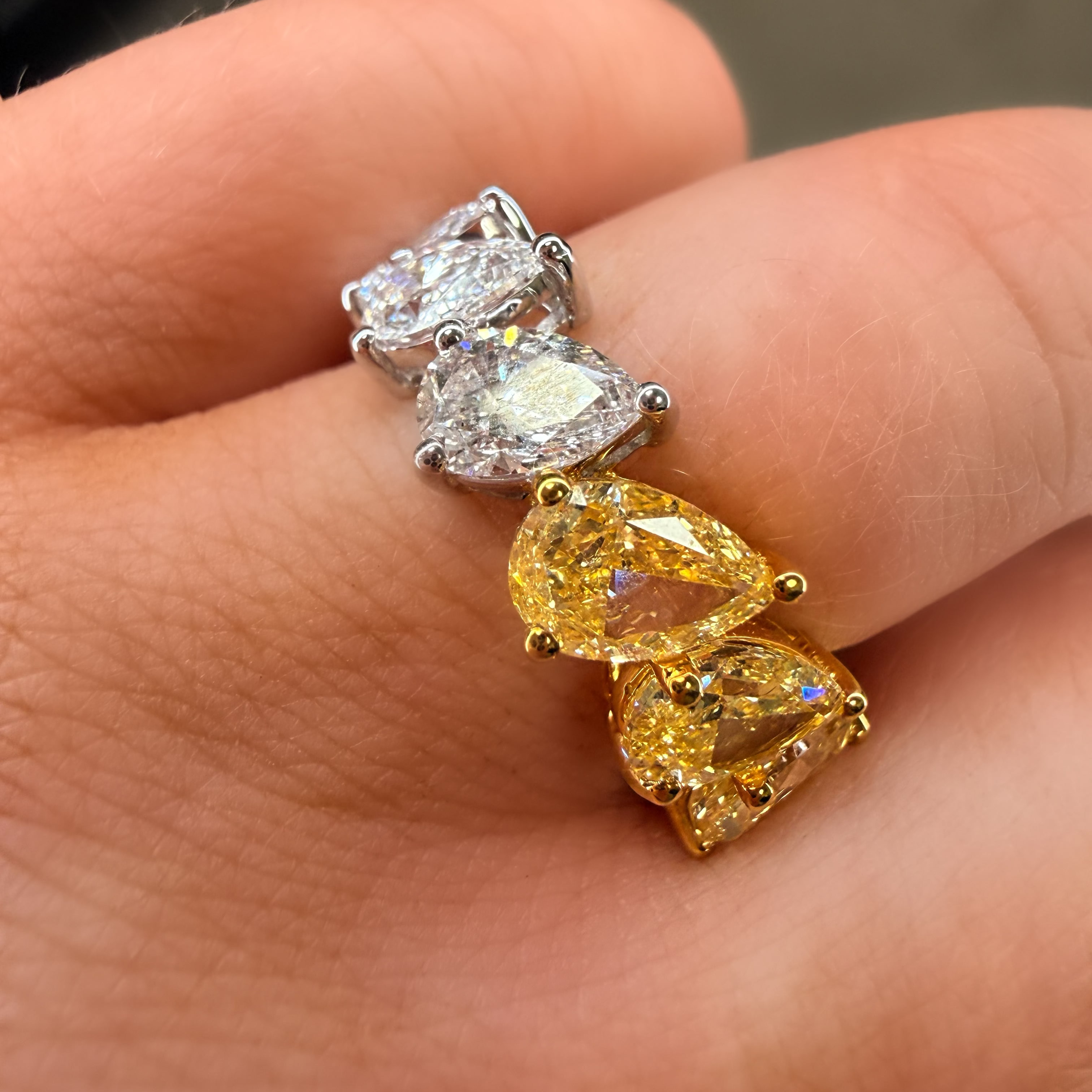 Two diamond rings being worn on fingers, one with yellow gemstones and the other with clear gemstones.