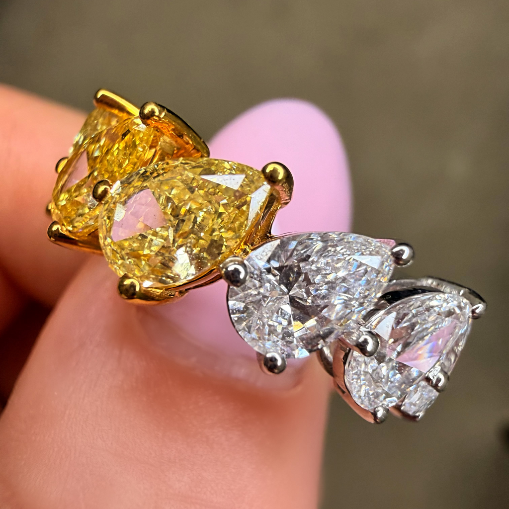 Two pairs of pear-shaped gemstone earrings, one gold and one silver, held between fingers against a neutral background.