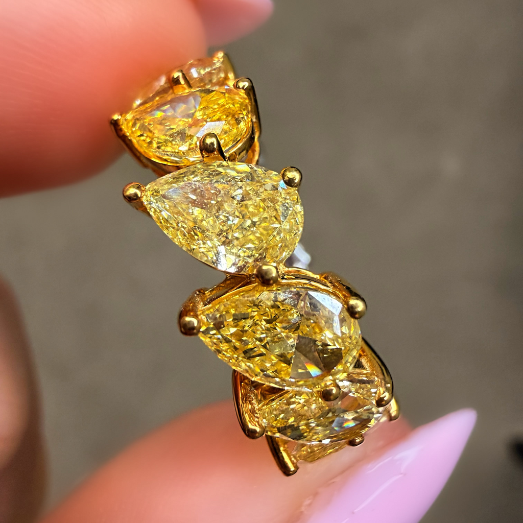 Gold earring with yellow gemstones held between fingers against a neutral background