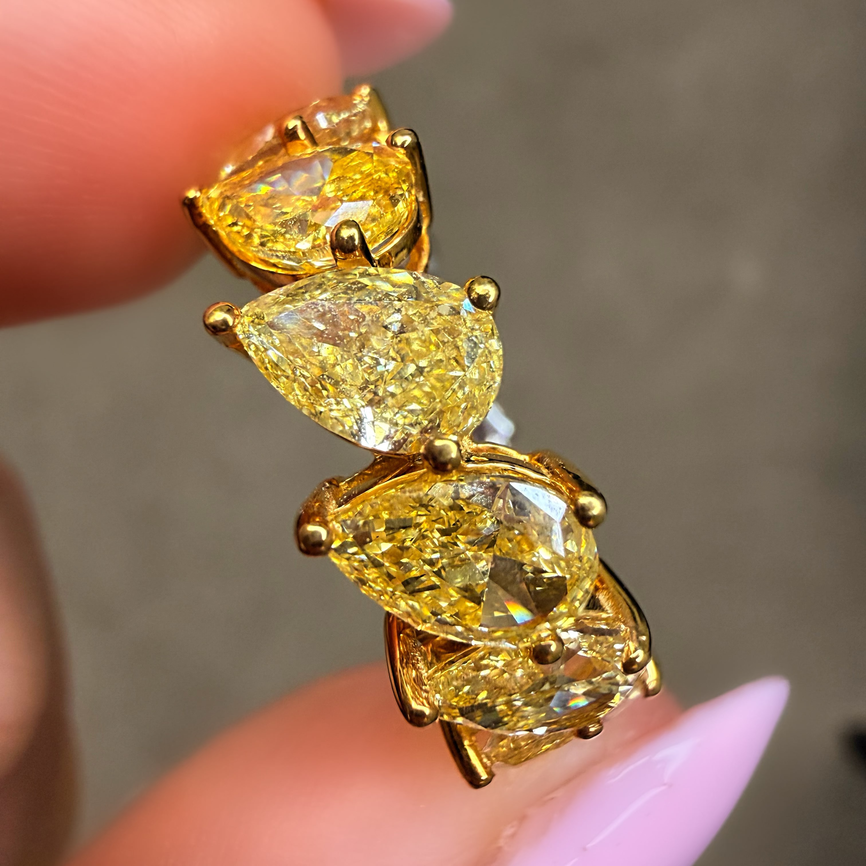 Gold earring with yellow gemstones held between fingers against a neutral background