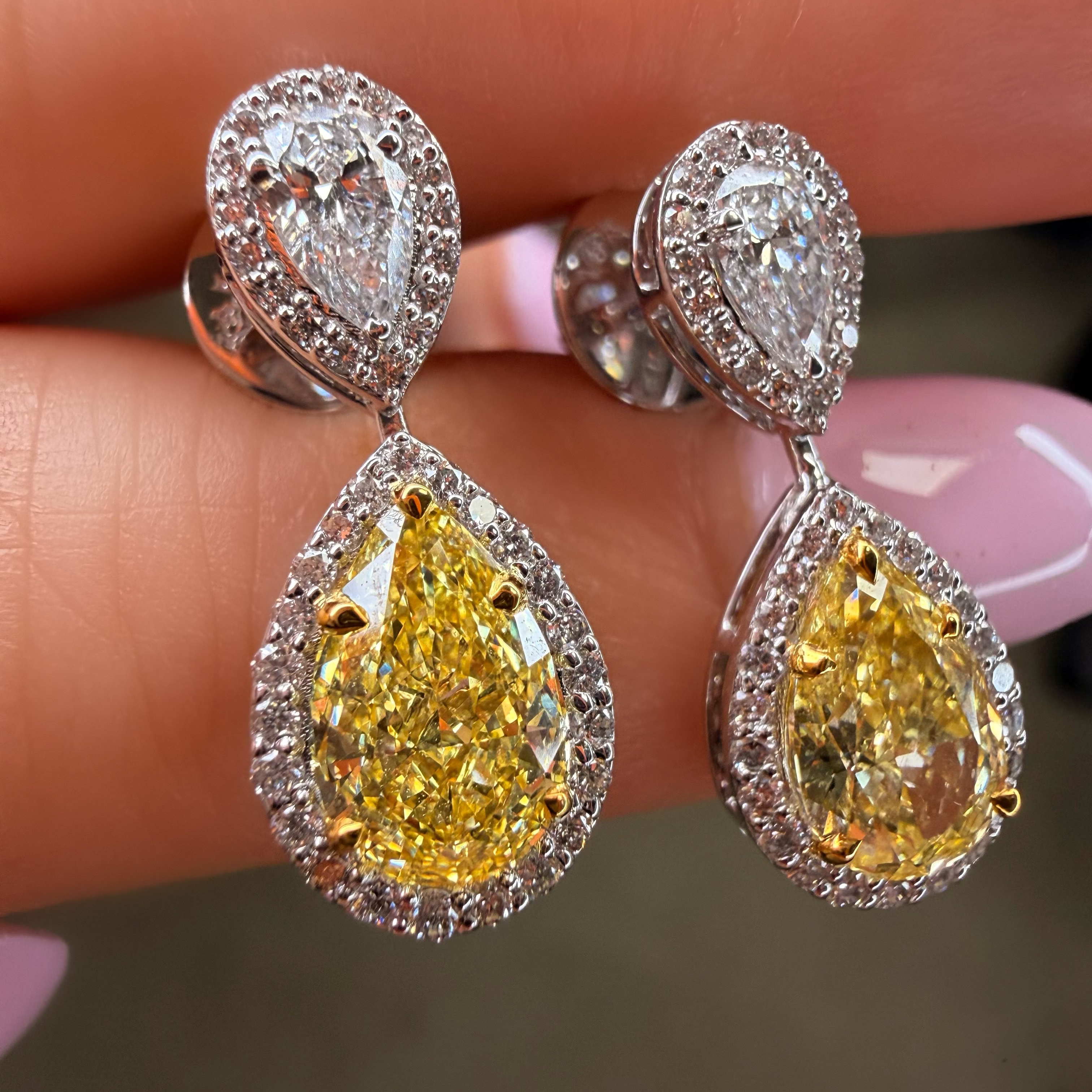Teardrop-shaped yellow gemstone earrings with silver detailing held between fingers.
