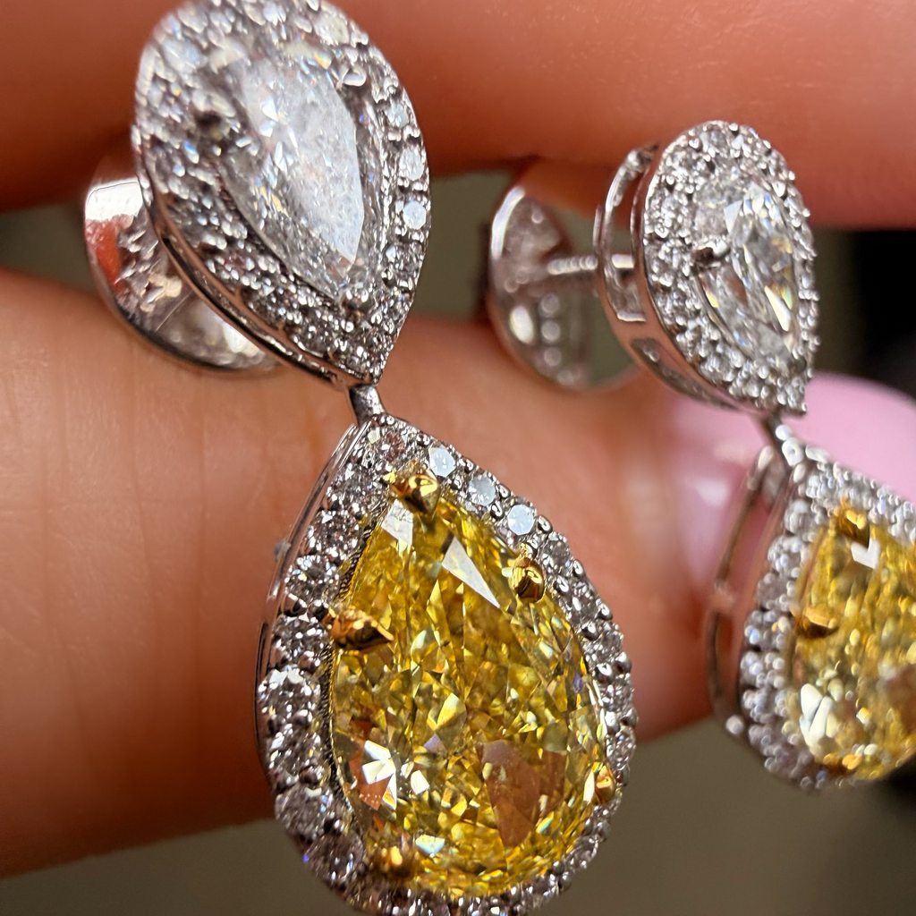 Close-up of yellow pear-shaped diamond earrings with silver prongs on a finger.