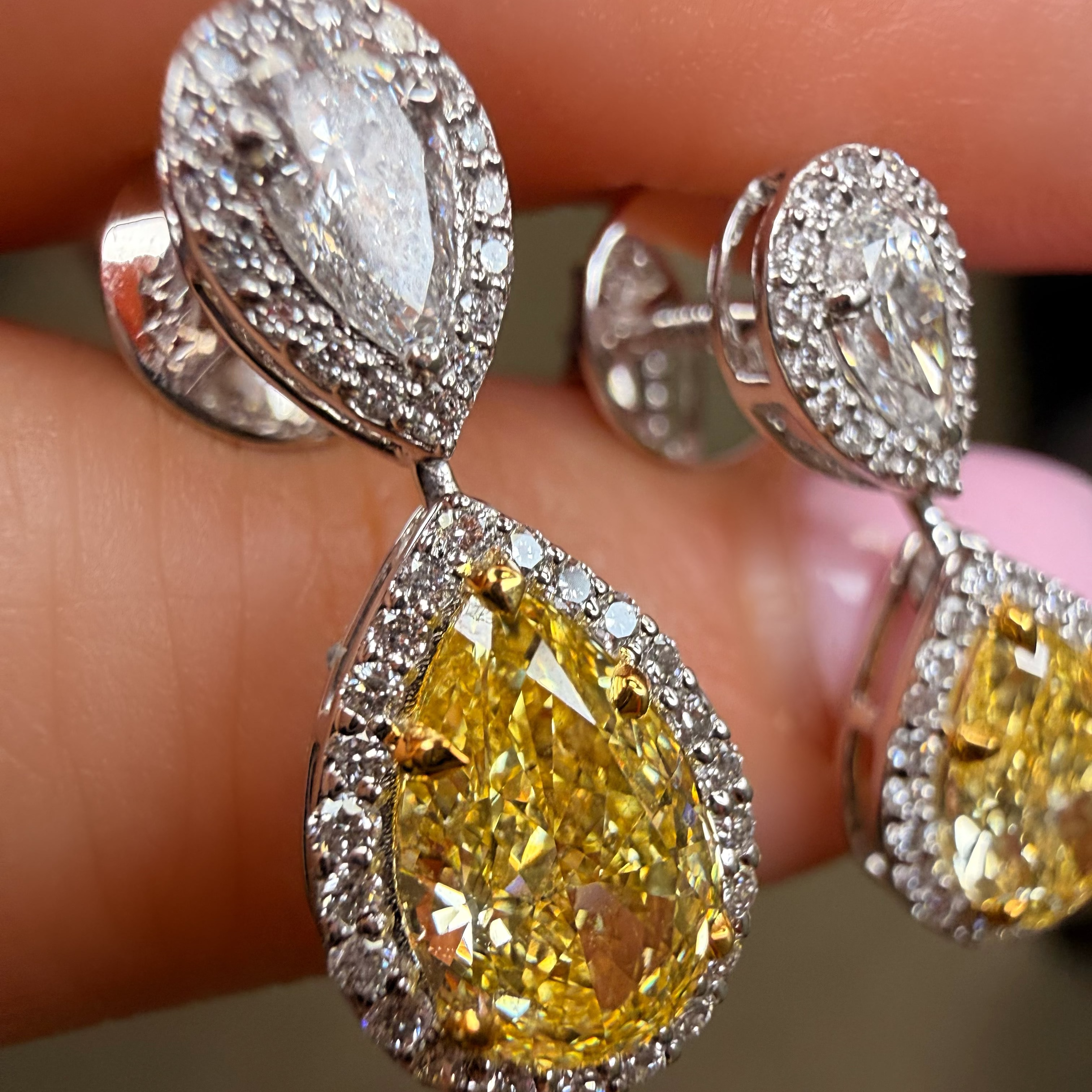 Close-up of yellow pear-shaped diamond earrings with silver prongs on a finger.
