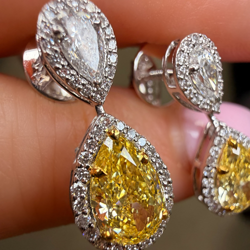 Close-up of yellow pear-shaped diamond earrings with silver prongs on a finger.