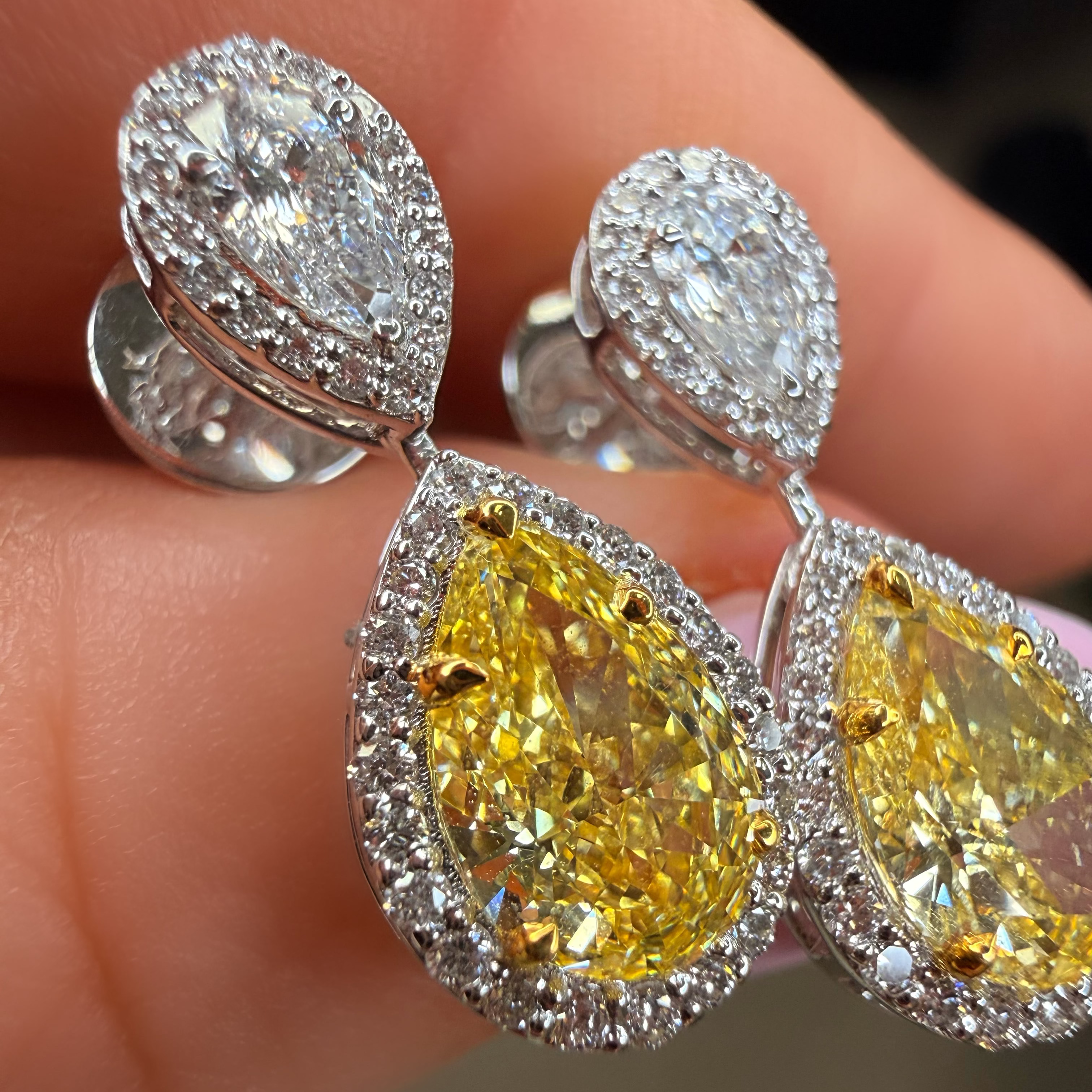 Close-up of yellow pear-shaped diamond earrings with silver settings held between fingers.