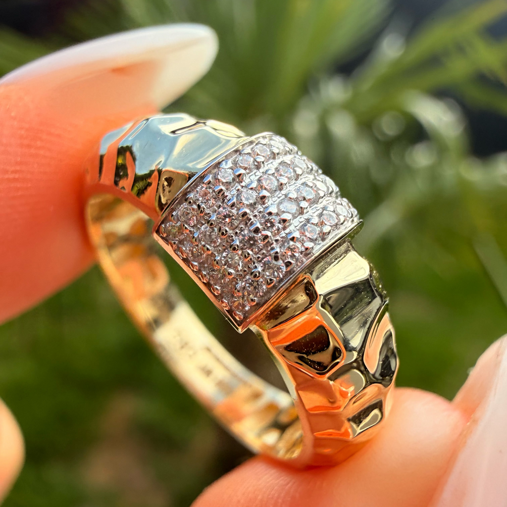 Gold ring with diamond accents held between fingers against a blurred natural background