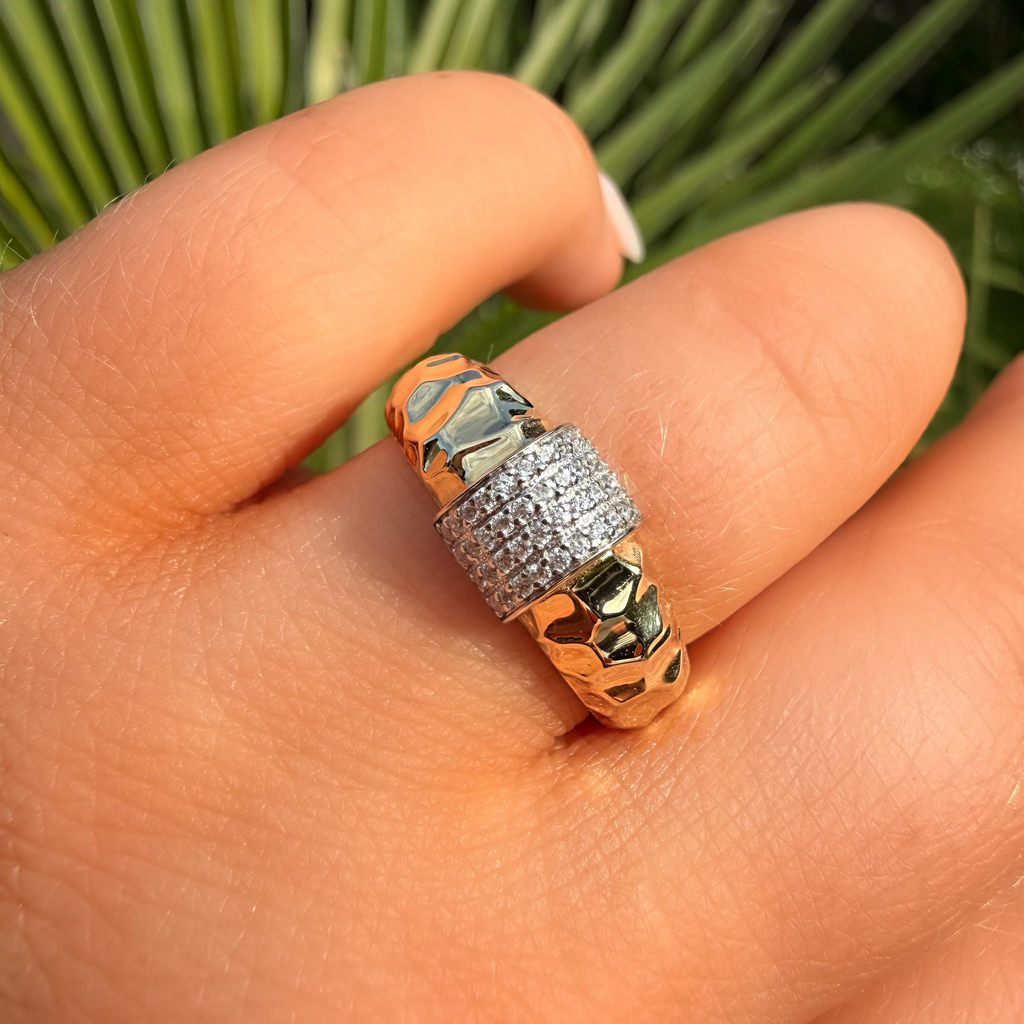 Gold ring with gemstones on a person's finger against a green plant background