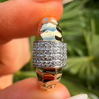 Silver ring with intricate design held between fingers against a blurred green background