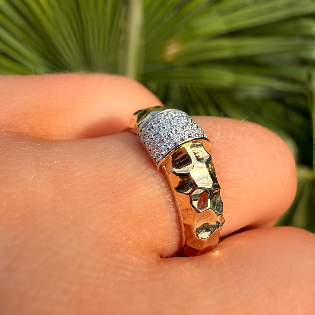 Gold ring with a face design on a finger against a green leafy background