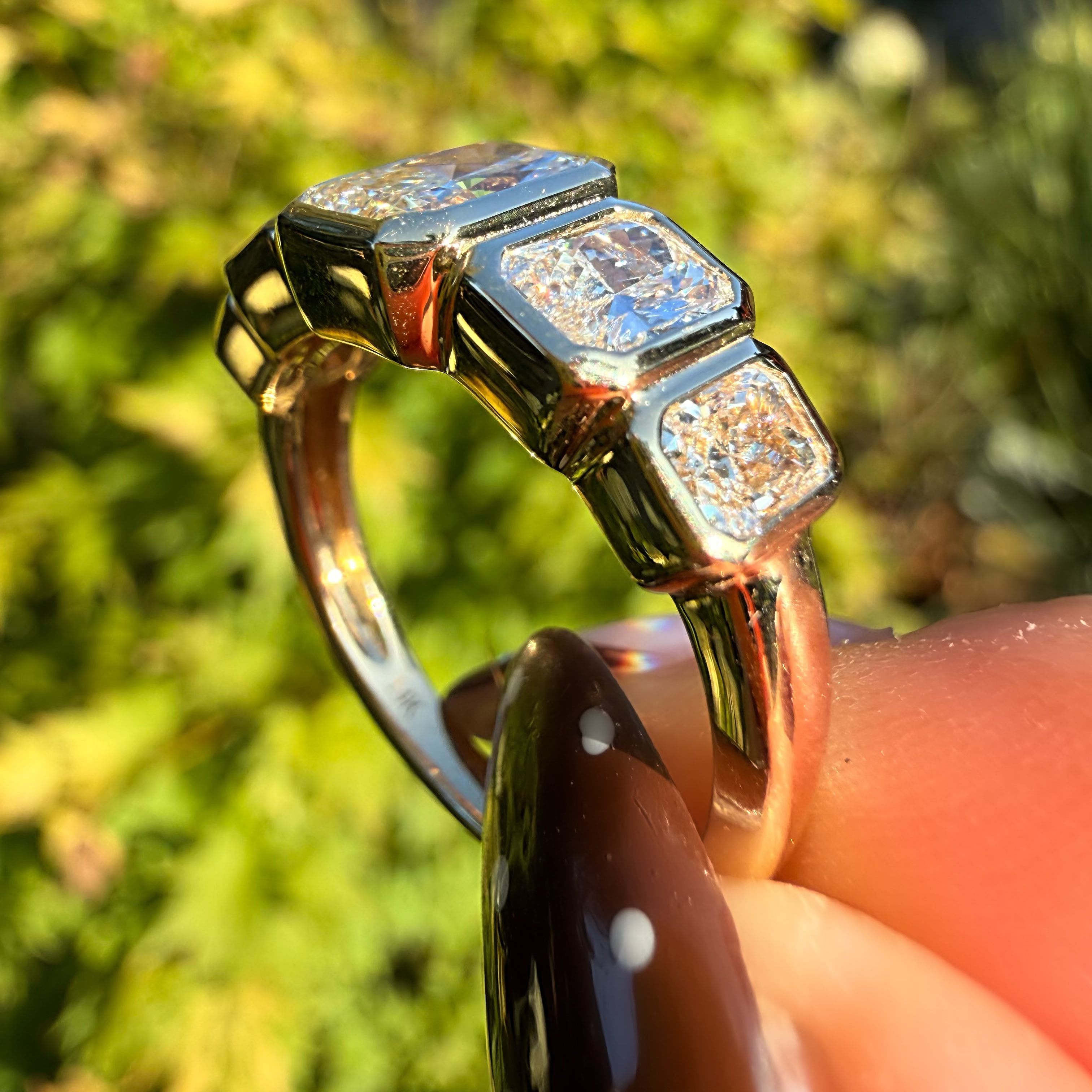 A close-up of a gold ring with three rectangular clear gemstones held by a hand against a blurred green outdoor background.