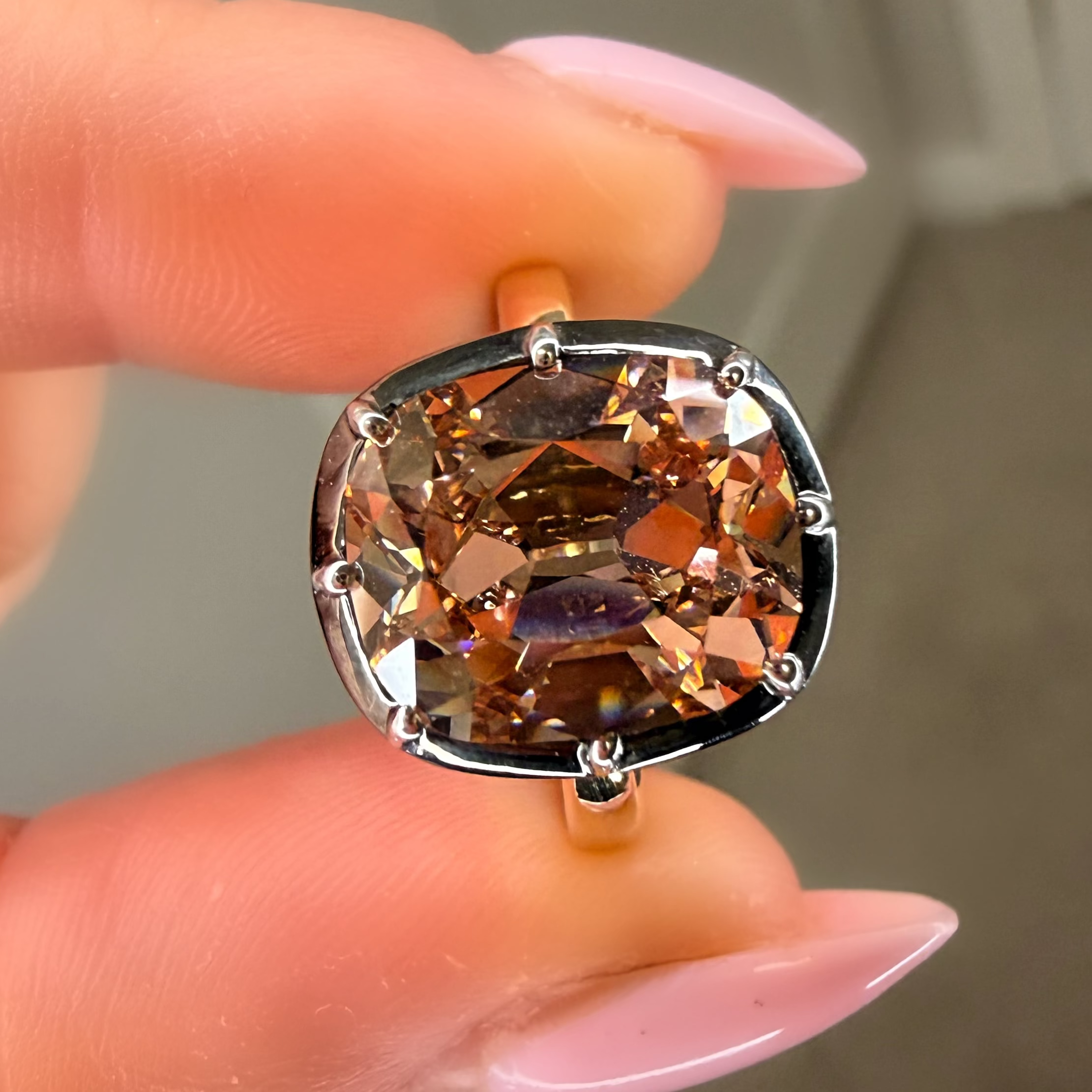 Ring with a large brown gemstone held between fingers against a neutral background