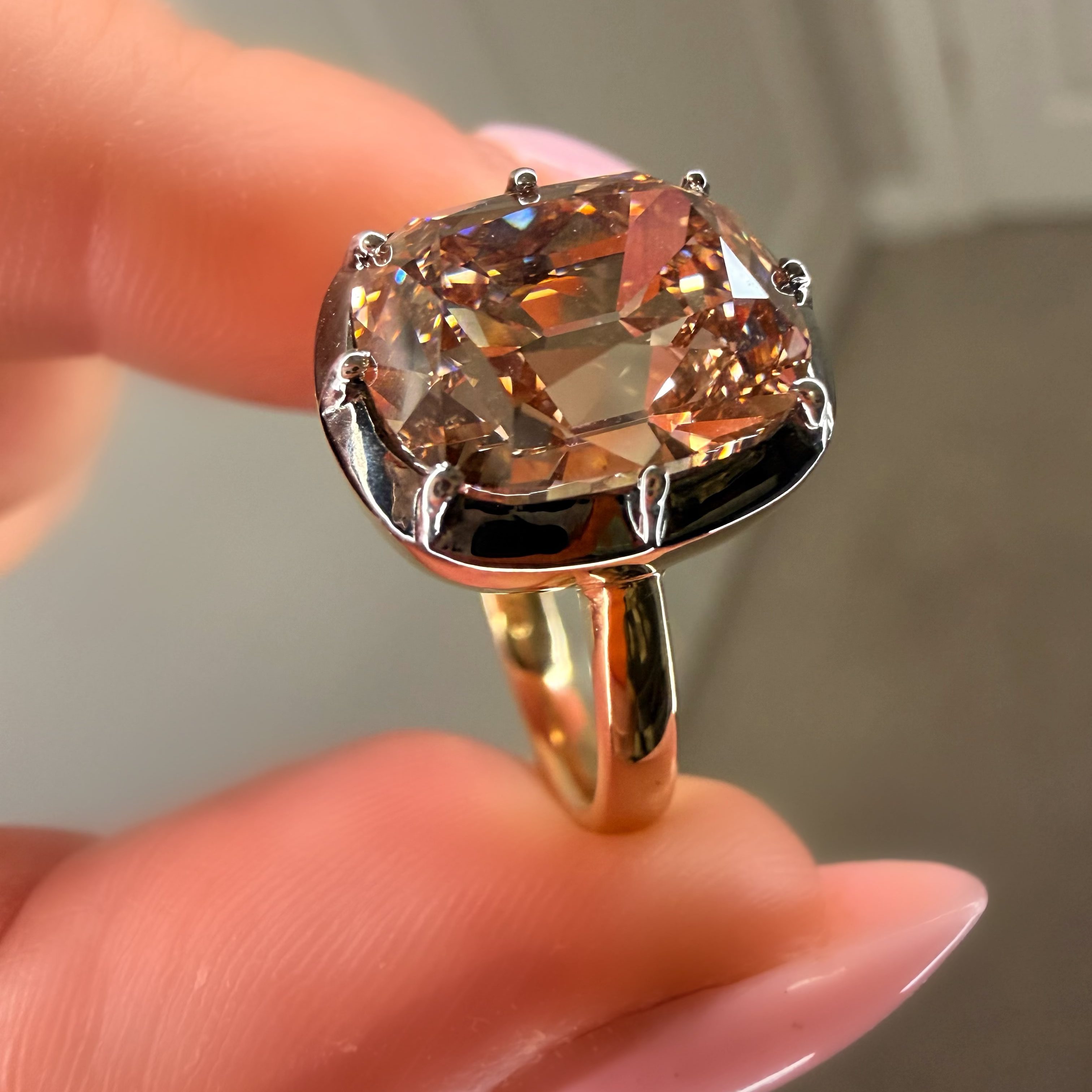 Gold ring with a large pinkish-brown gemstone held by a hand against a neutral background