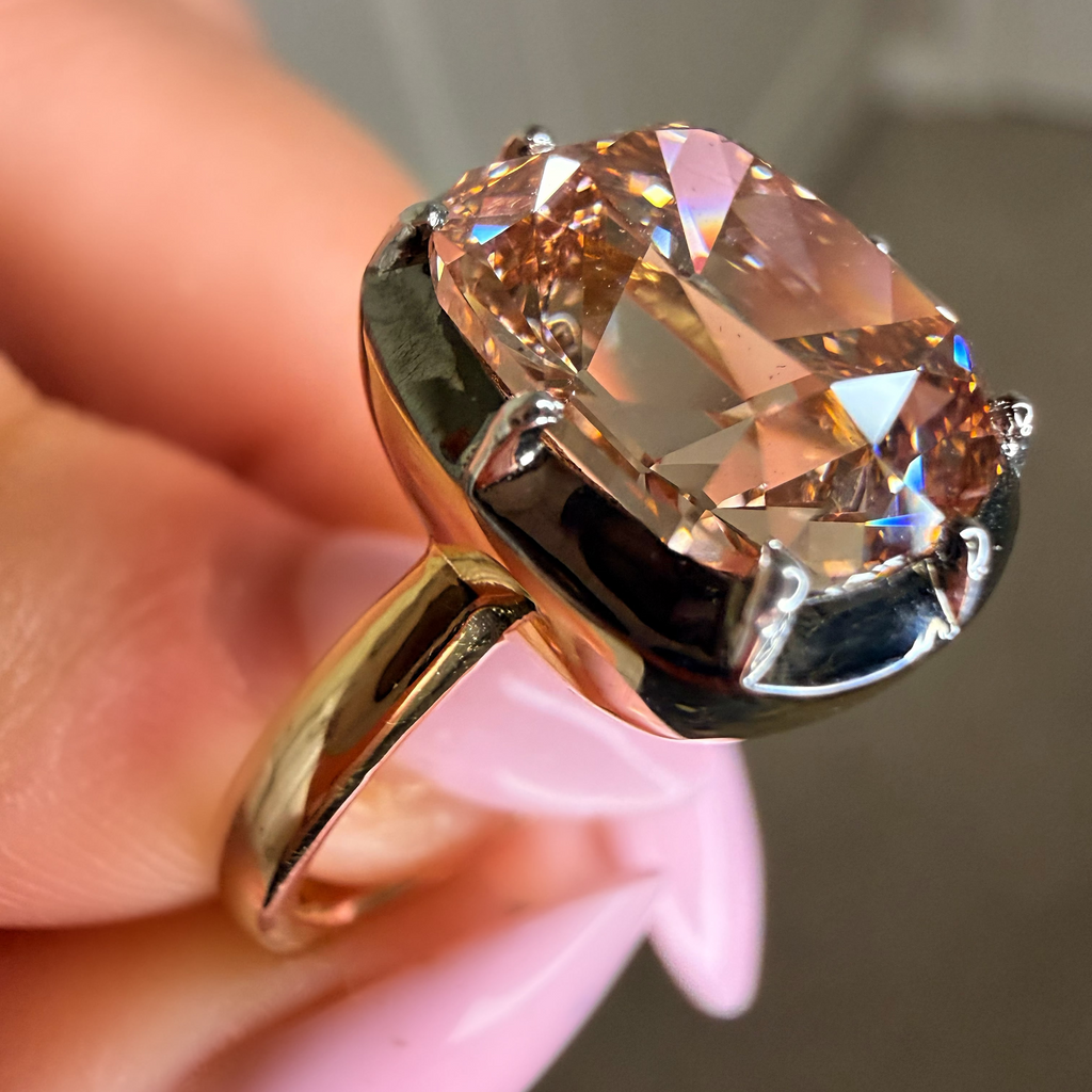 Gold ring with a large pink gemstone held by a hand against a neutral background