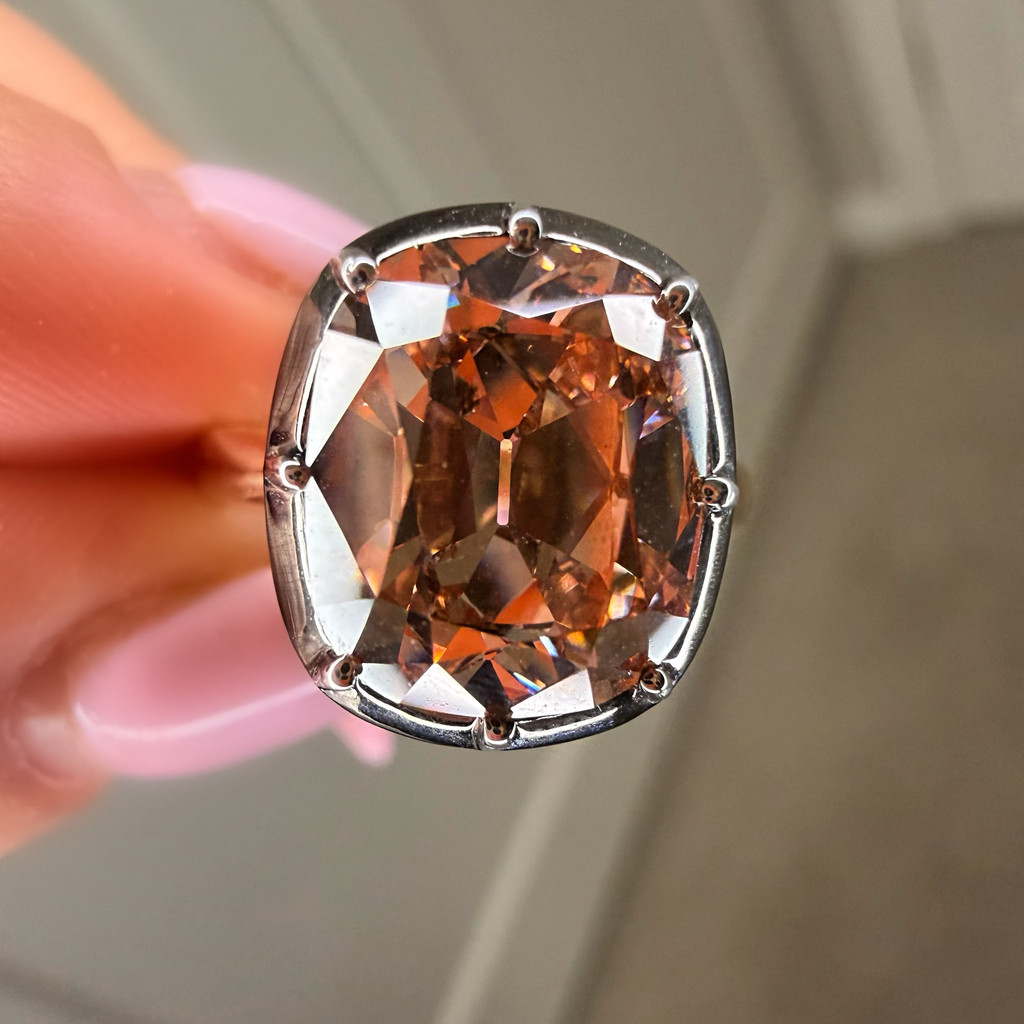 Brown gemstone in a silver setting held by a hand against a neutral background