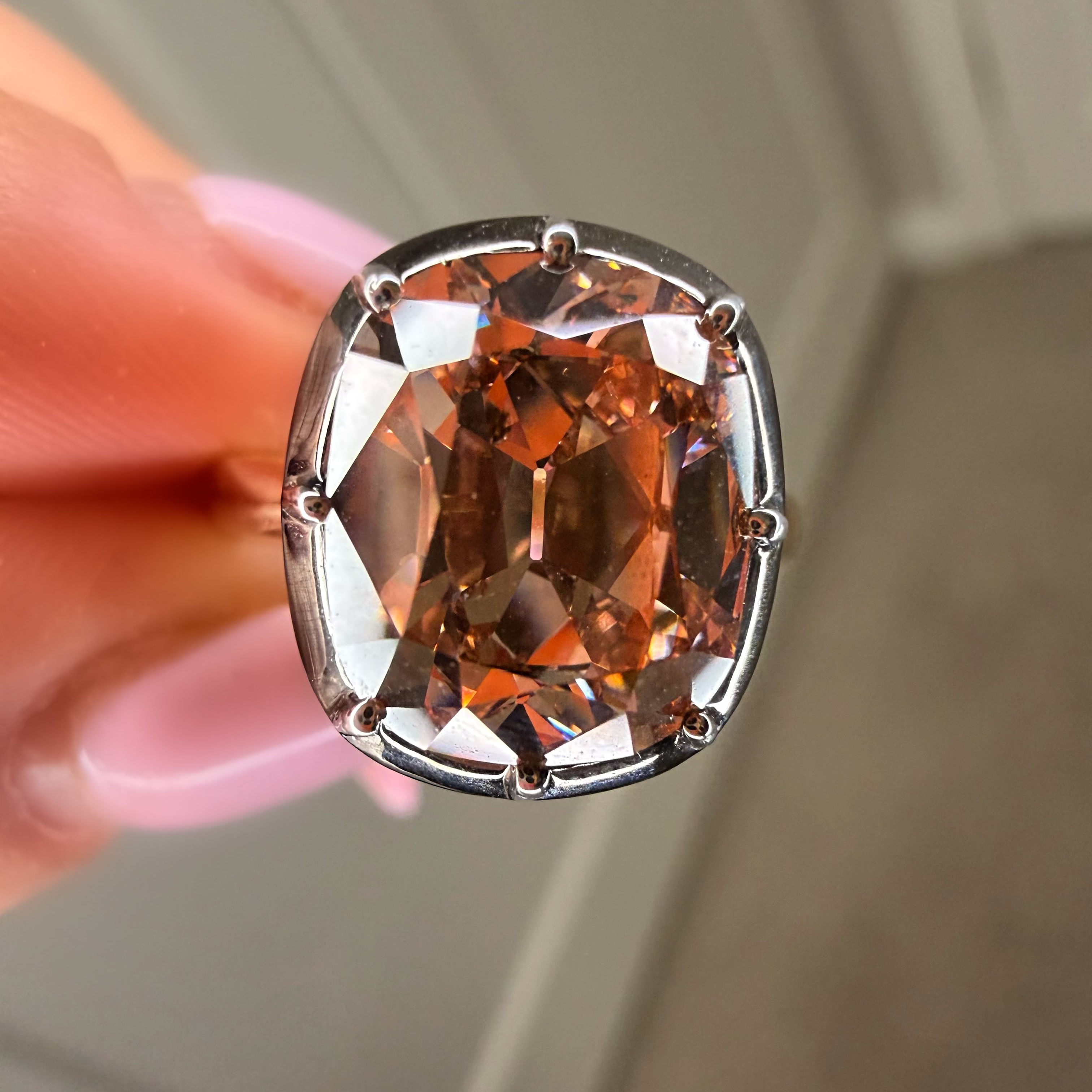 Brown gemstone in a silver setting held by a hand against a neutral background