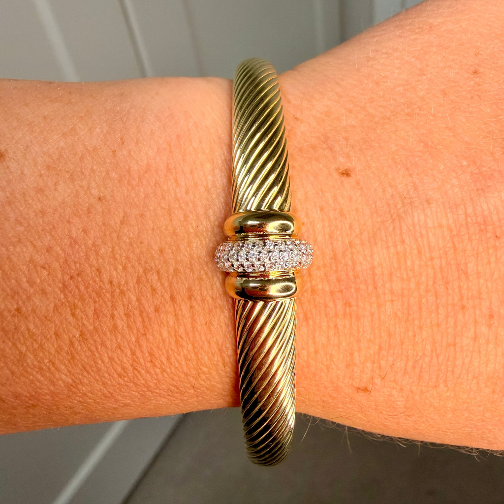 Gold bracelet with diamond accents on a wrist against a neutral background