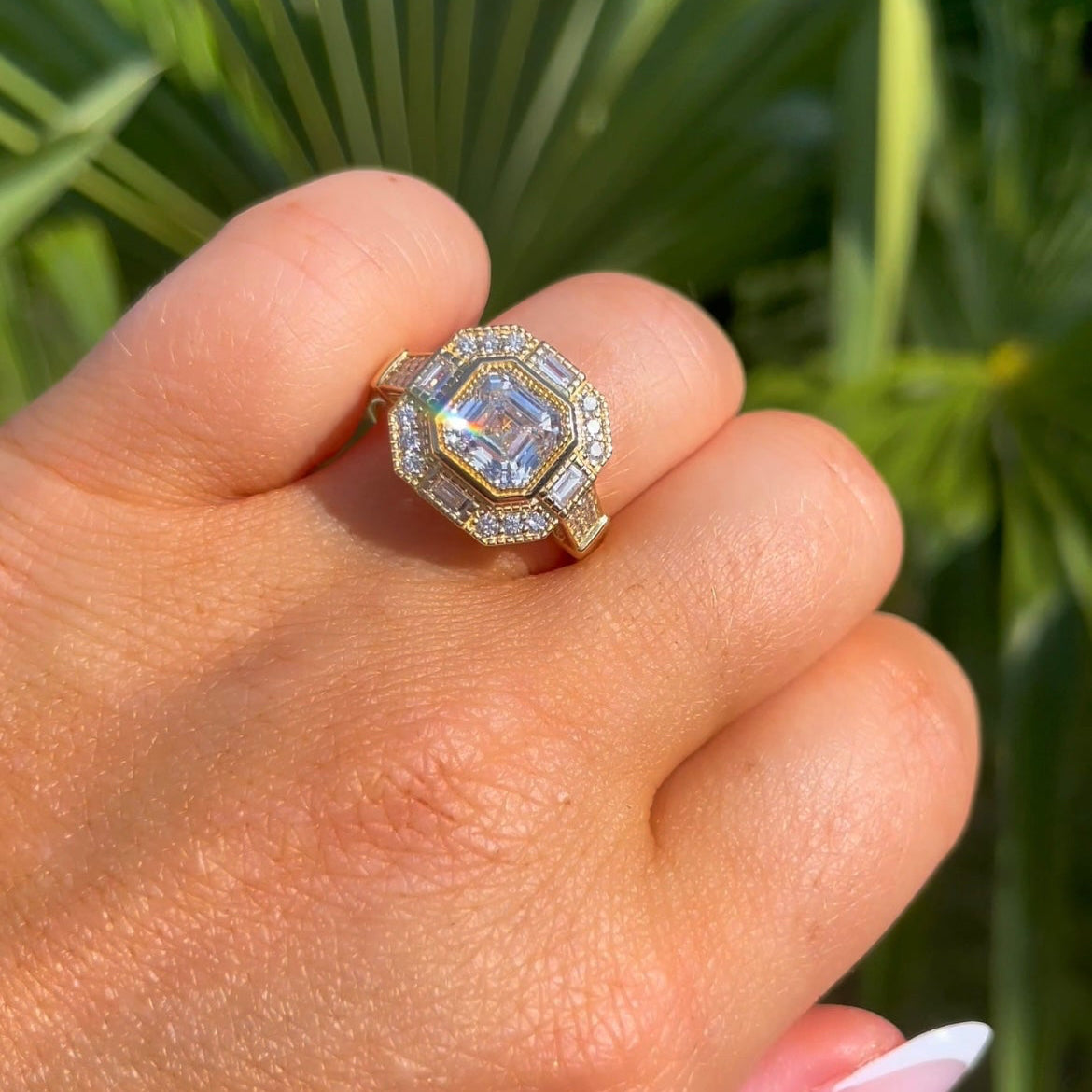 Hand wearing a diamond ring with a green leafy background