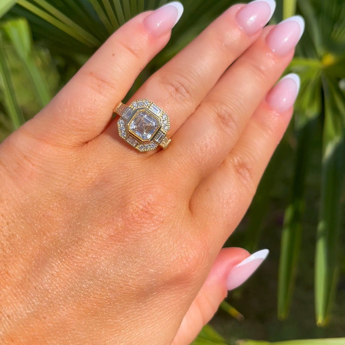 Hand wearing a diamond ring with a green leafy background