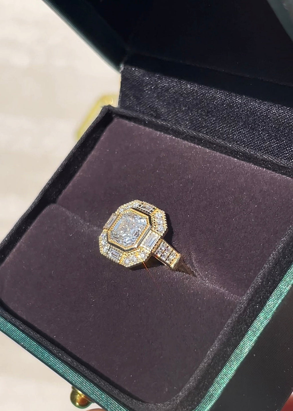 Diamond ring in a black velvet box held by a hand with pink nail polish.