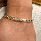 A close-up of a person's wrist wearing a twisted rope-style bracelet with alternating gold and diamond-encrusted segments.