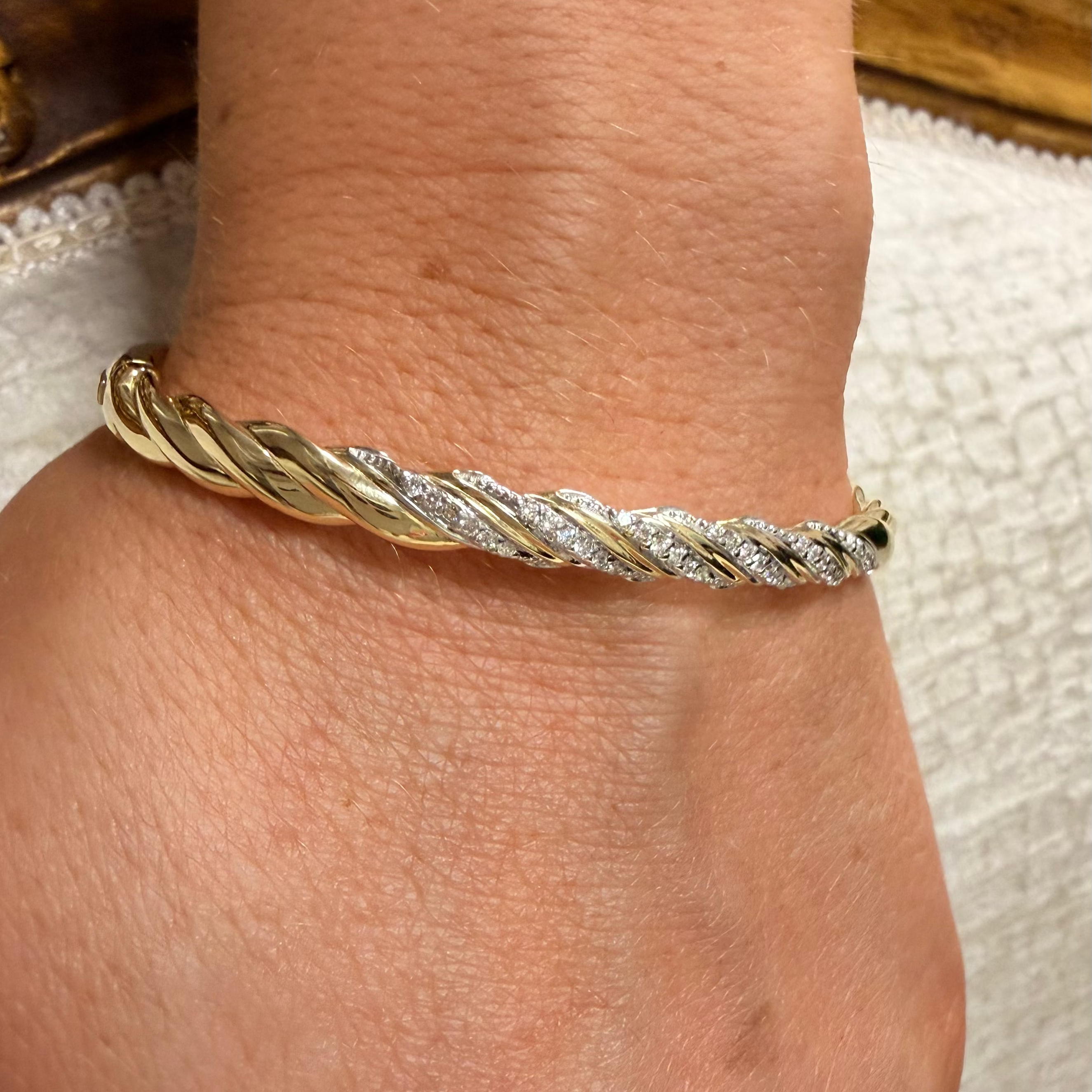 A close-up of a person's wrist wearing a twisted rope-style bracelet with alternating gold and diamond-encrusted segments.