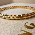 Gold bracelet on a textured beige surface with 'V' branding.