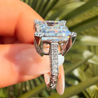 Diamond ring held by a hand with a blurred green leafy background