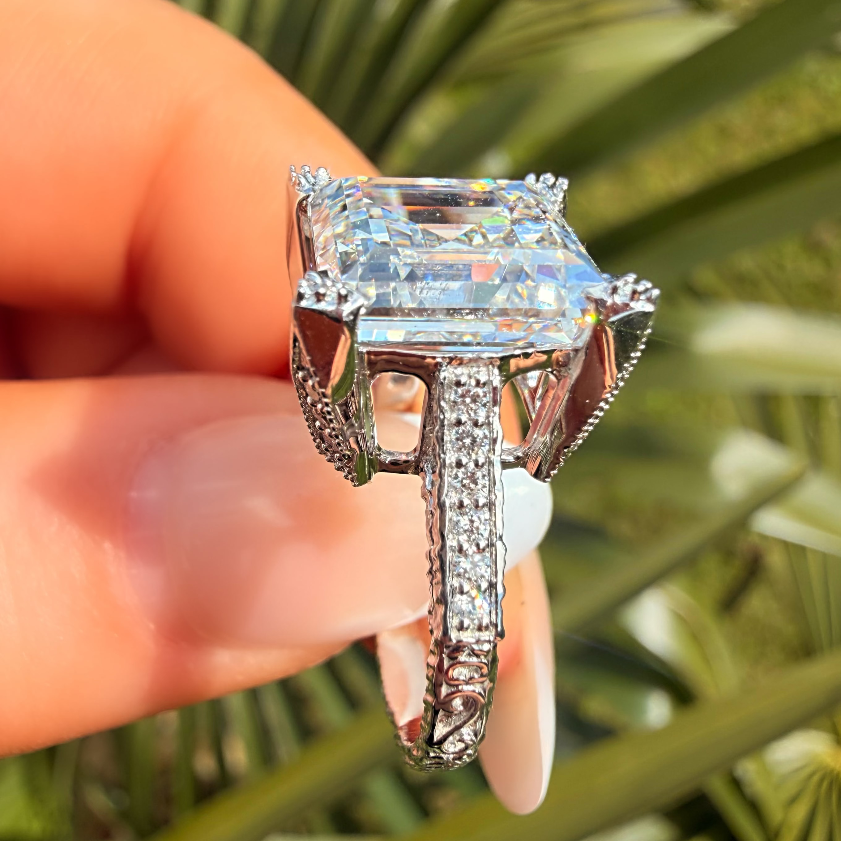 Diamond ring held by a hand with a blurred green leafy background