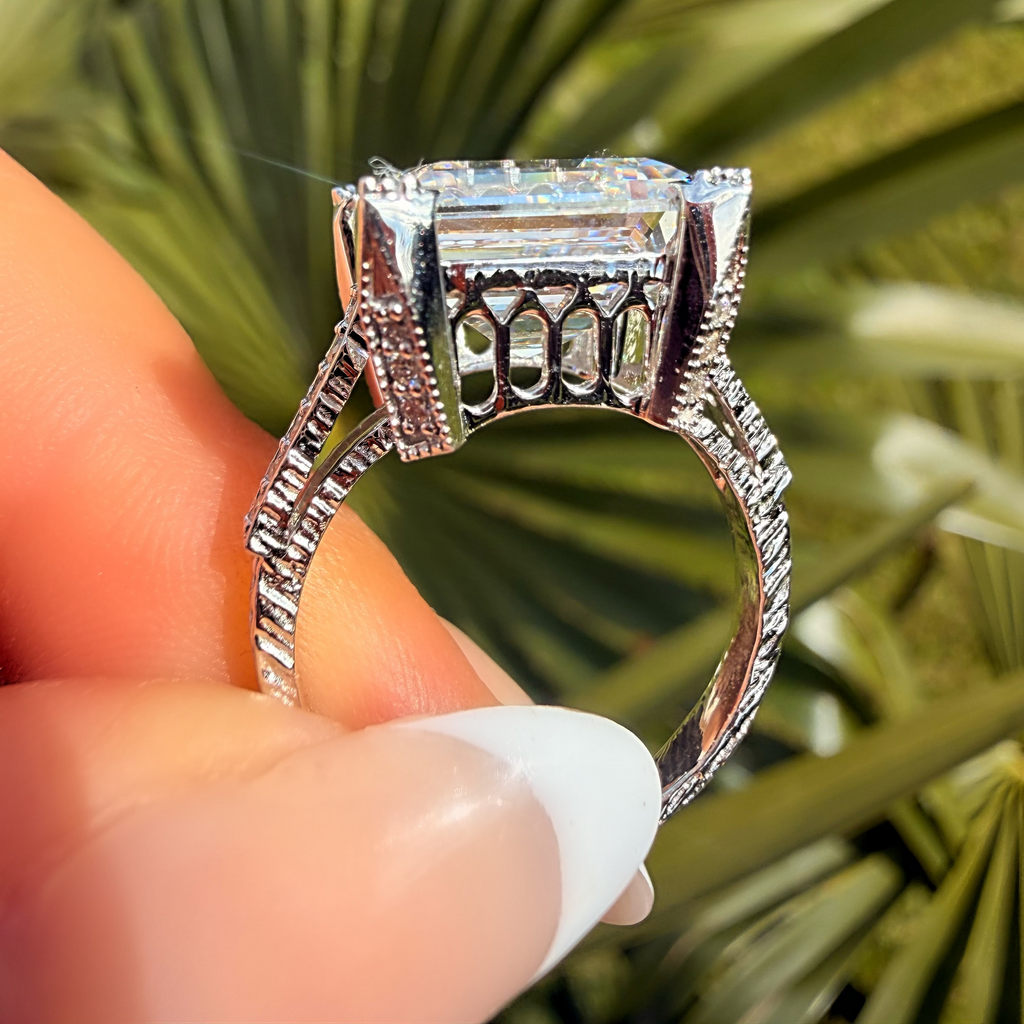 Silver ring with a large diamond held between fingers against a blurred green plant background