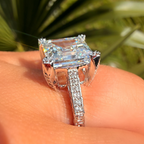 Silver ring with a large diamond on a person's finger, blurred green background