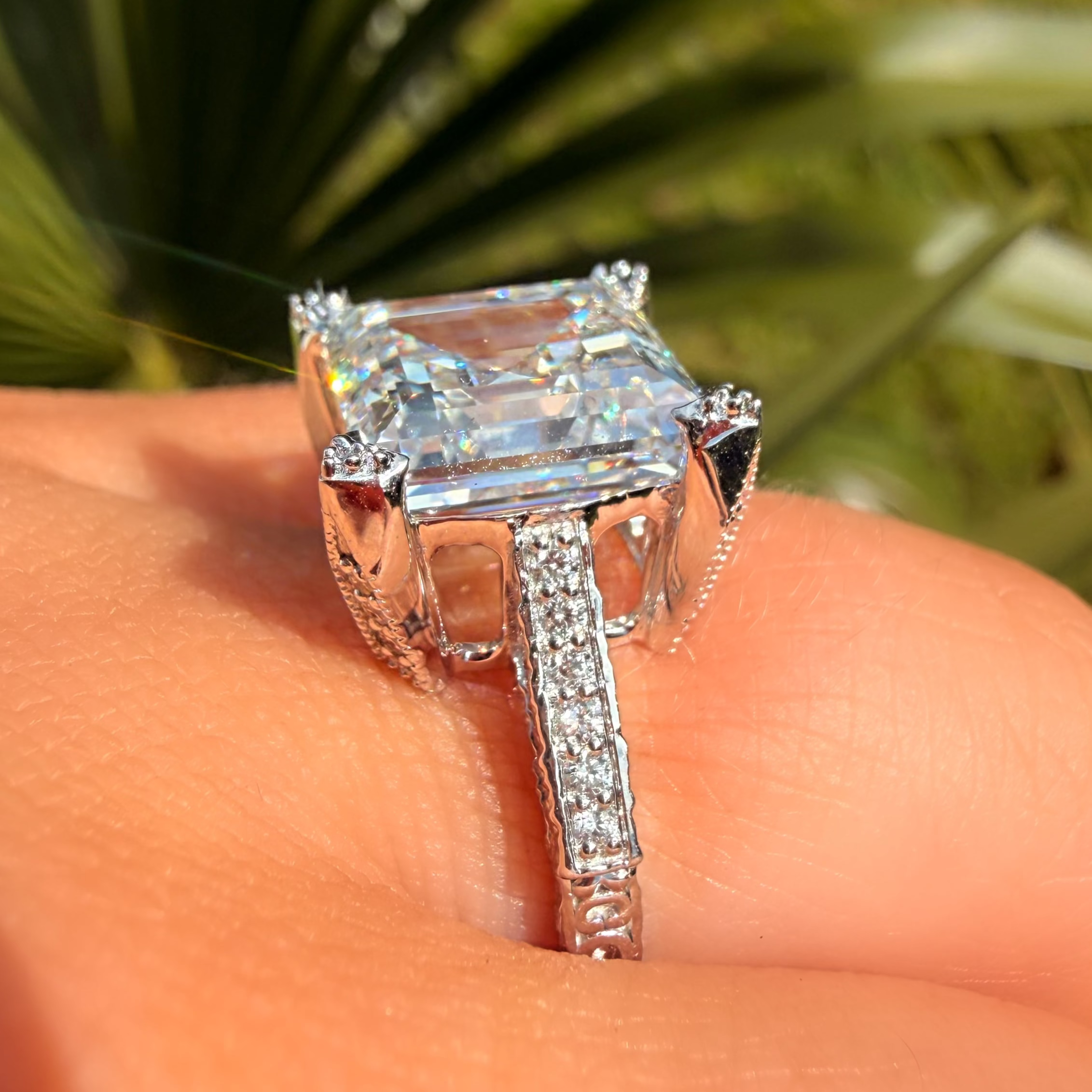 Silver ring with a large diamond on a person's finger, blurred green background