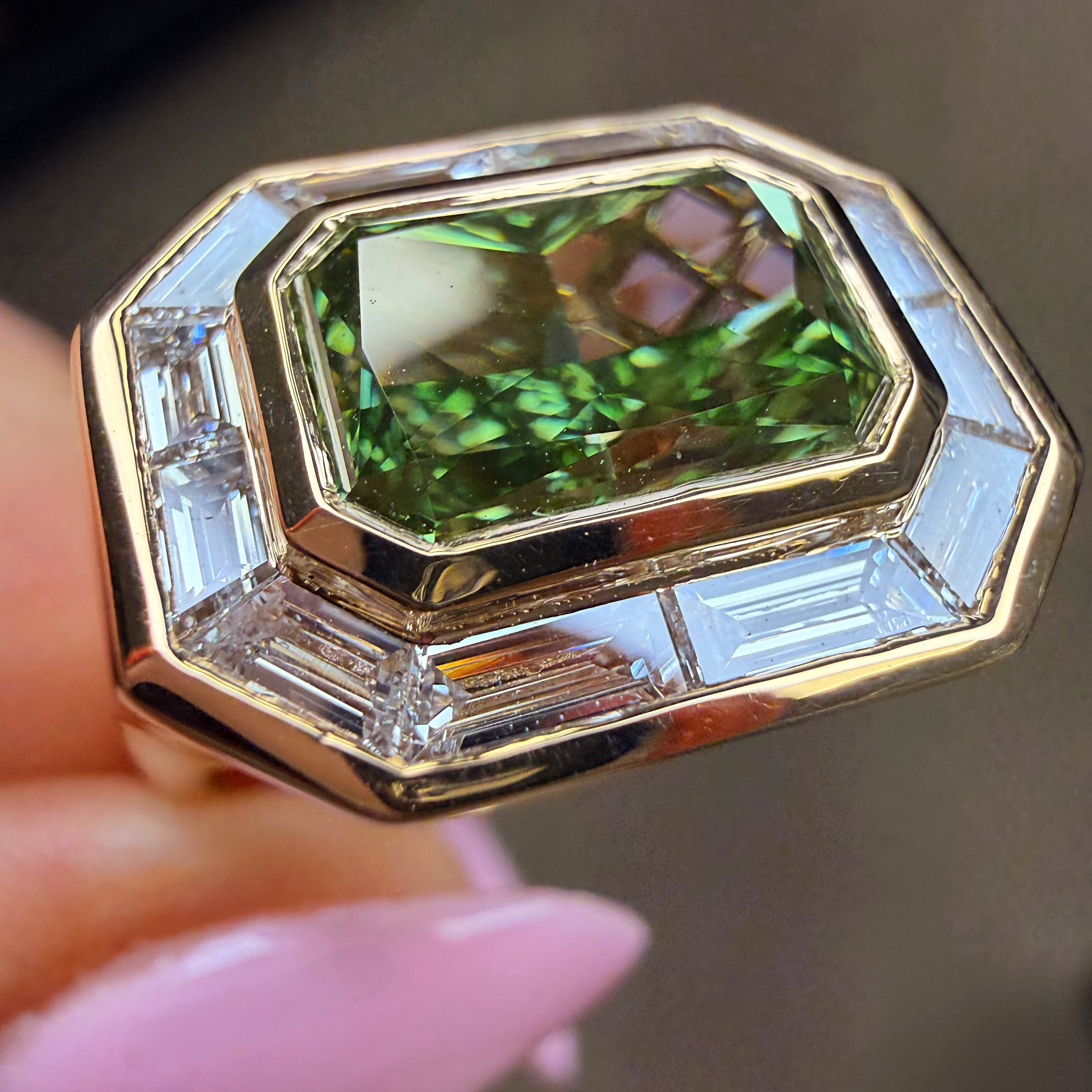 Gold ring with a green gemstone held by a hand with pink nail polish.