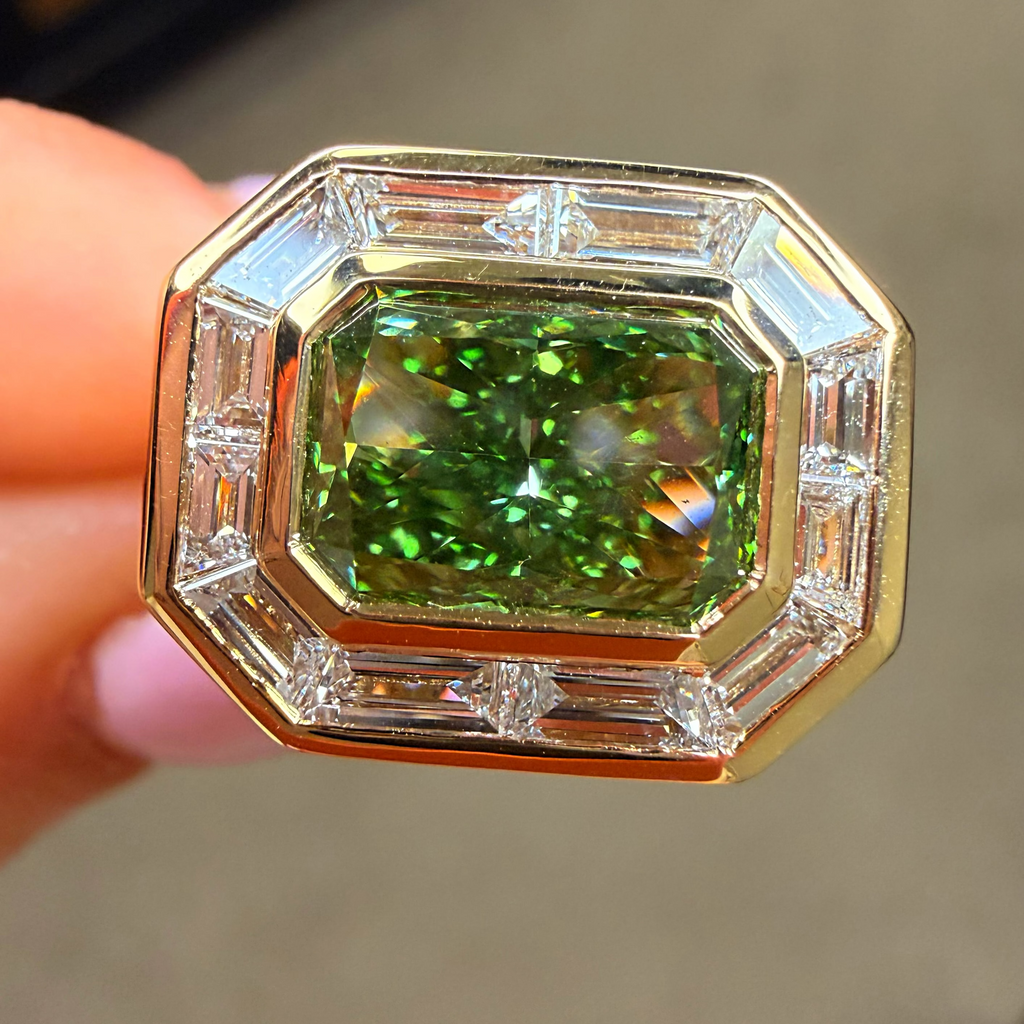 Gold ring with a green gemstone and diamond accents held by a hand.
