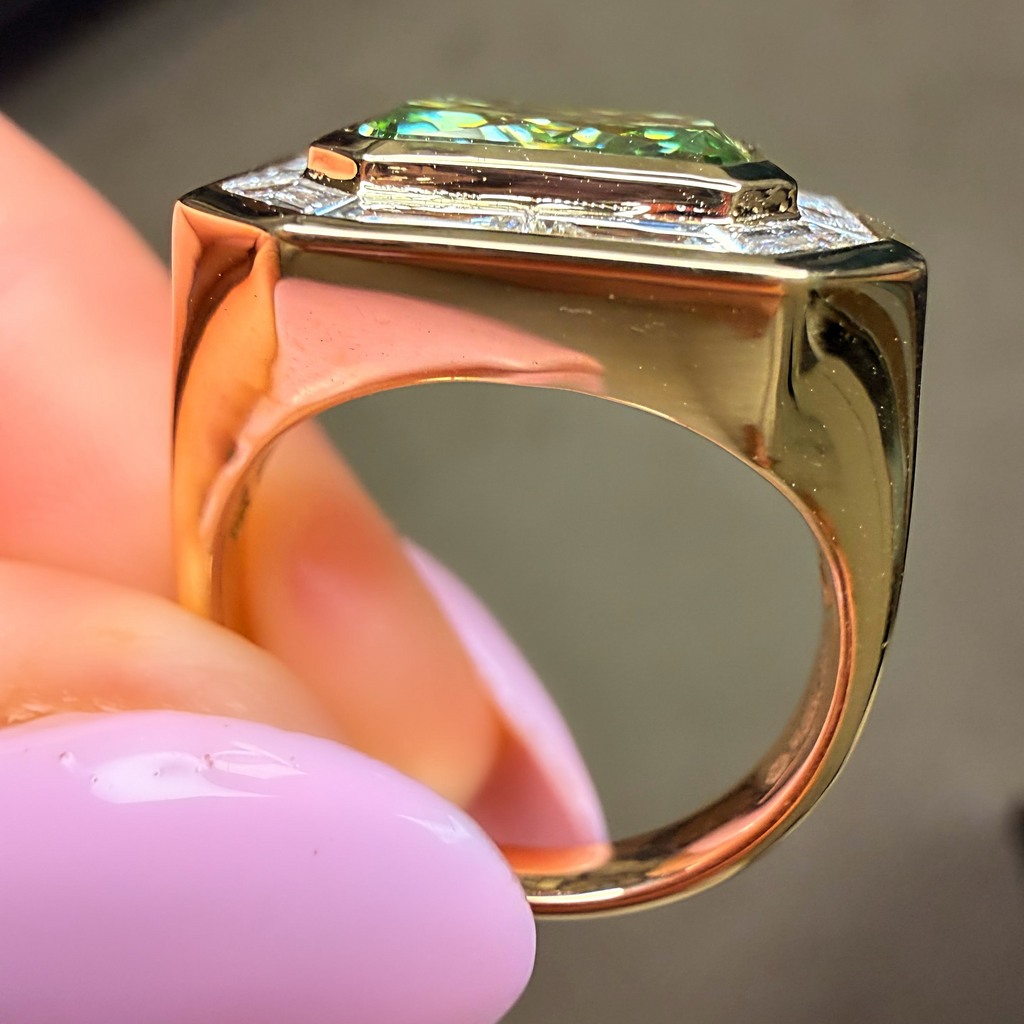 Gold ring with a green gemstone held by a hand with pink nail polish.