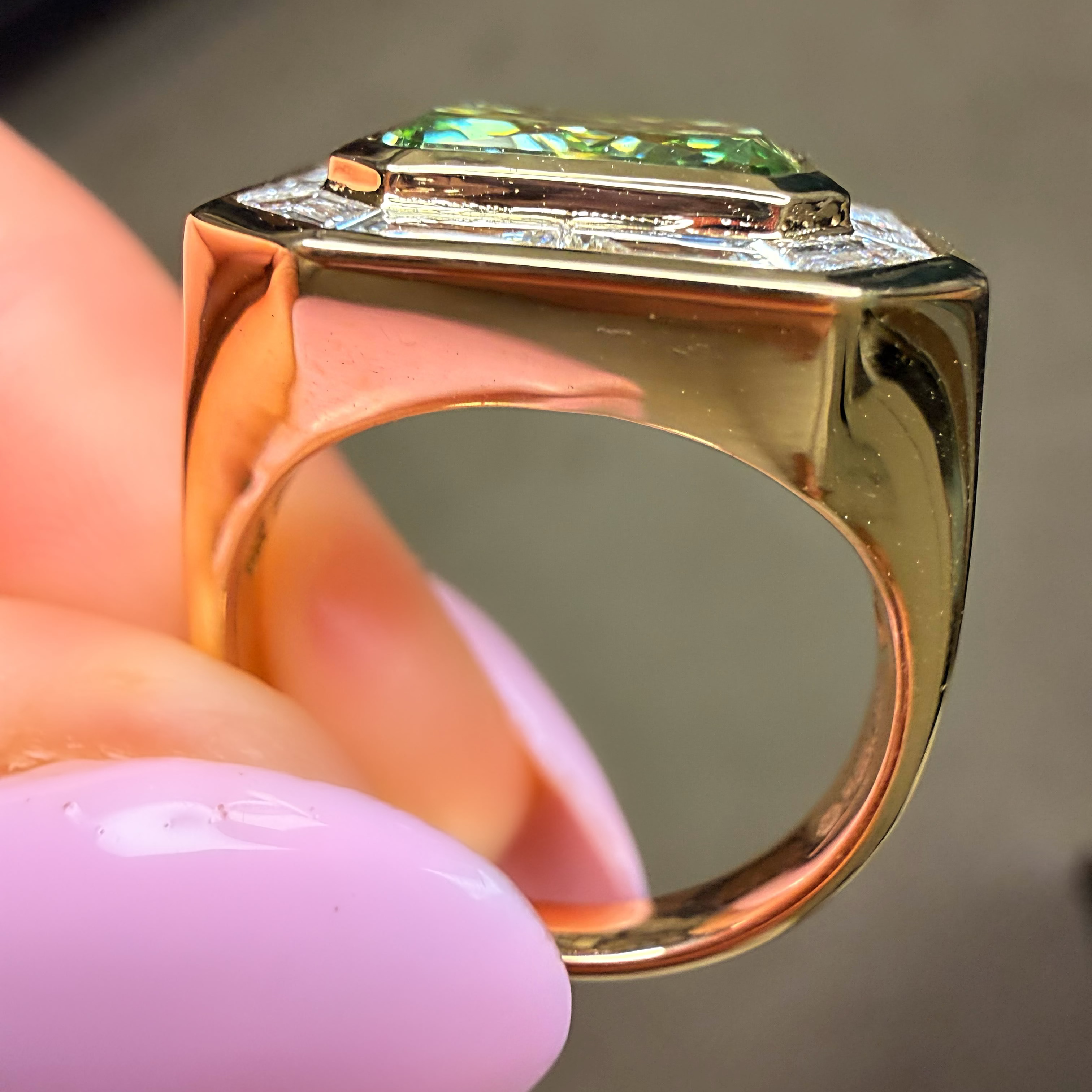 Gold ring with a green gemstone held by a hand with pink nail polish.