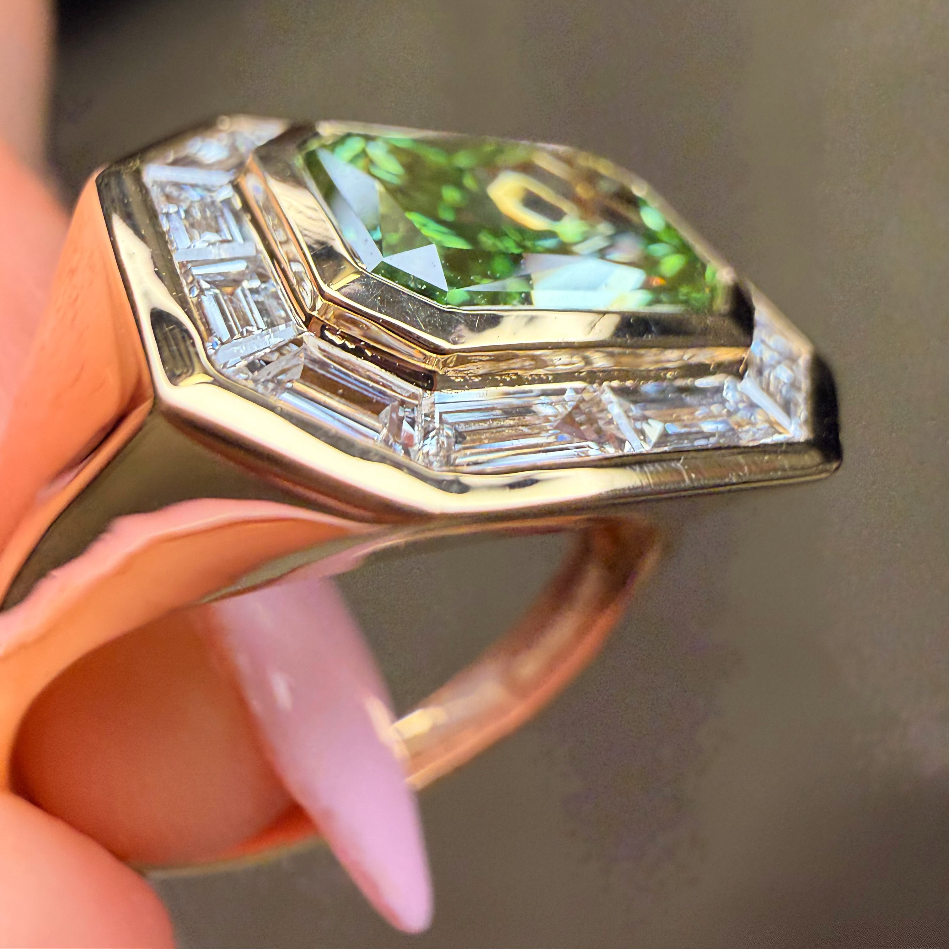 Gold ring with a green gemstone held by a hand against a neutral background