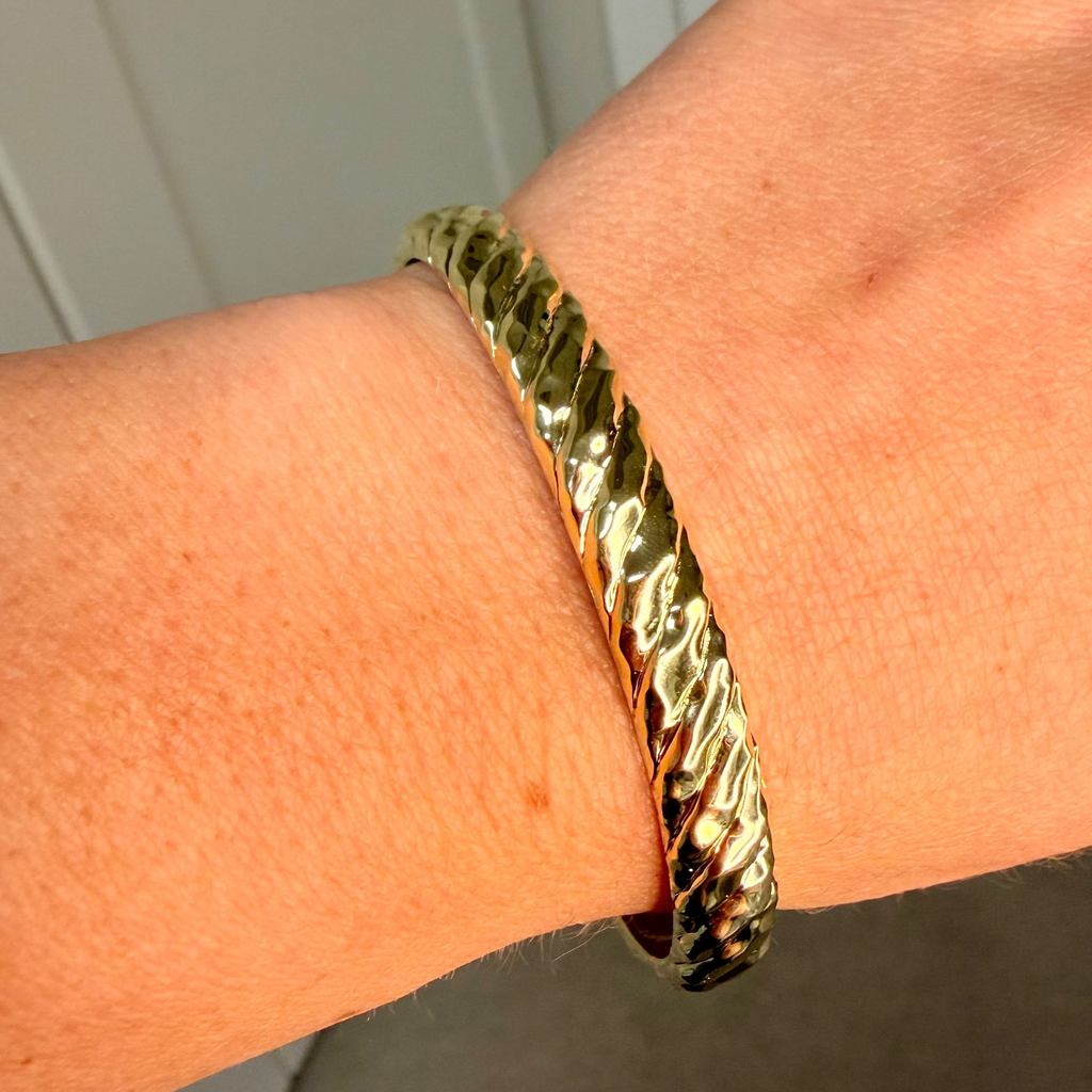 Gold bracelet on a wrist with a neutral background