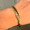 Gold bracelet on a wrist with a neutral background