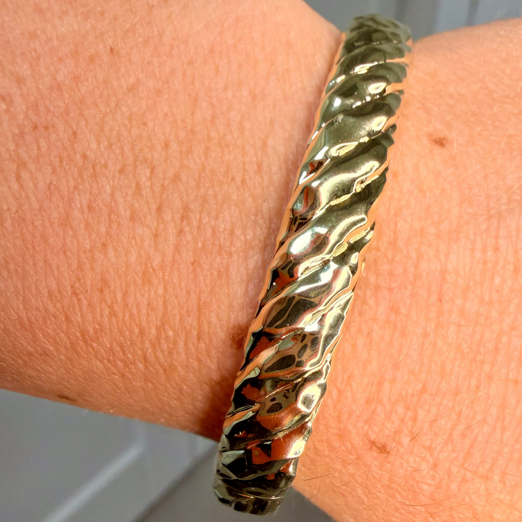 Gold bracelet on a wrist with a neutral background
