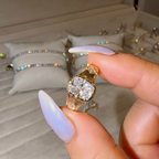 Gold ring with a large diamond held by a hand in front of a jewelry display.
