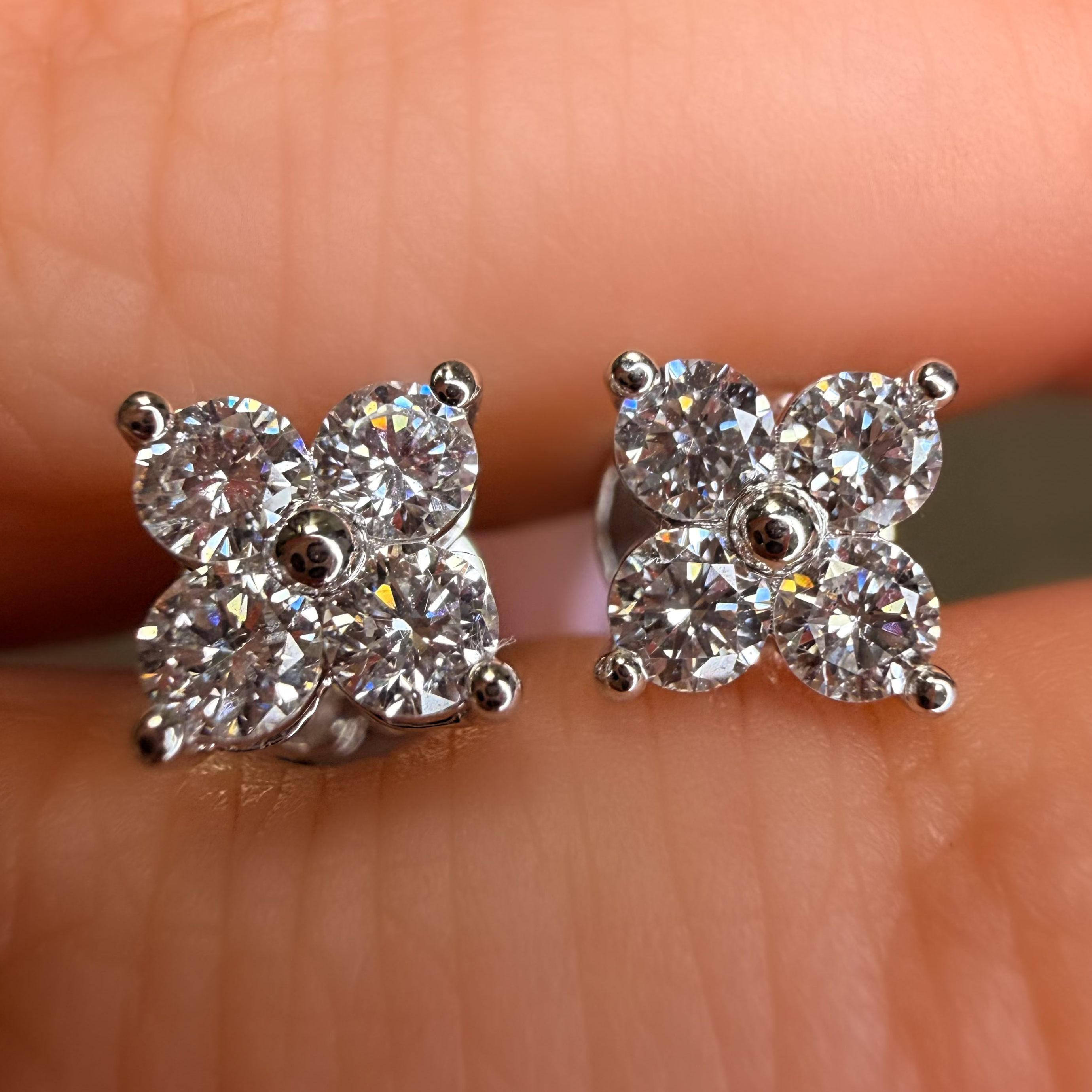Diamond stud earrings held between fingers against a neutral background