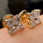 Gold flower-shaped earrings with clear gemstones on a person's ear.