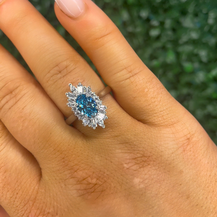 Hand wearing a ring with a blue gemstone against a green textured background