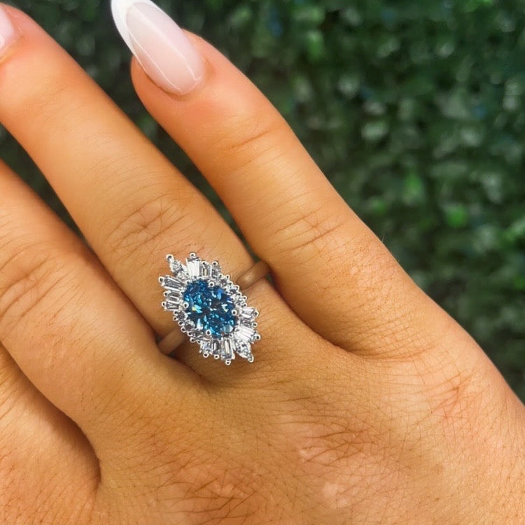 Ring with a blue gemstone on a finger against a green leafy background