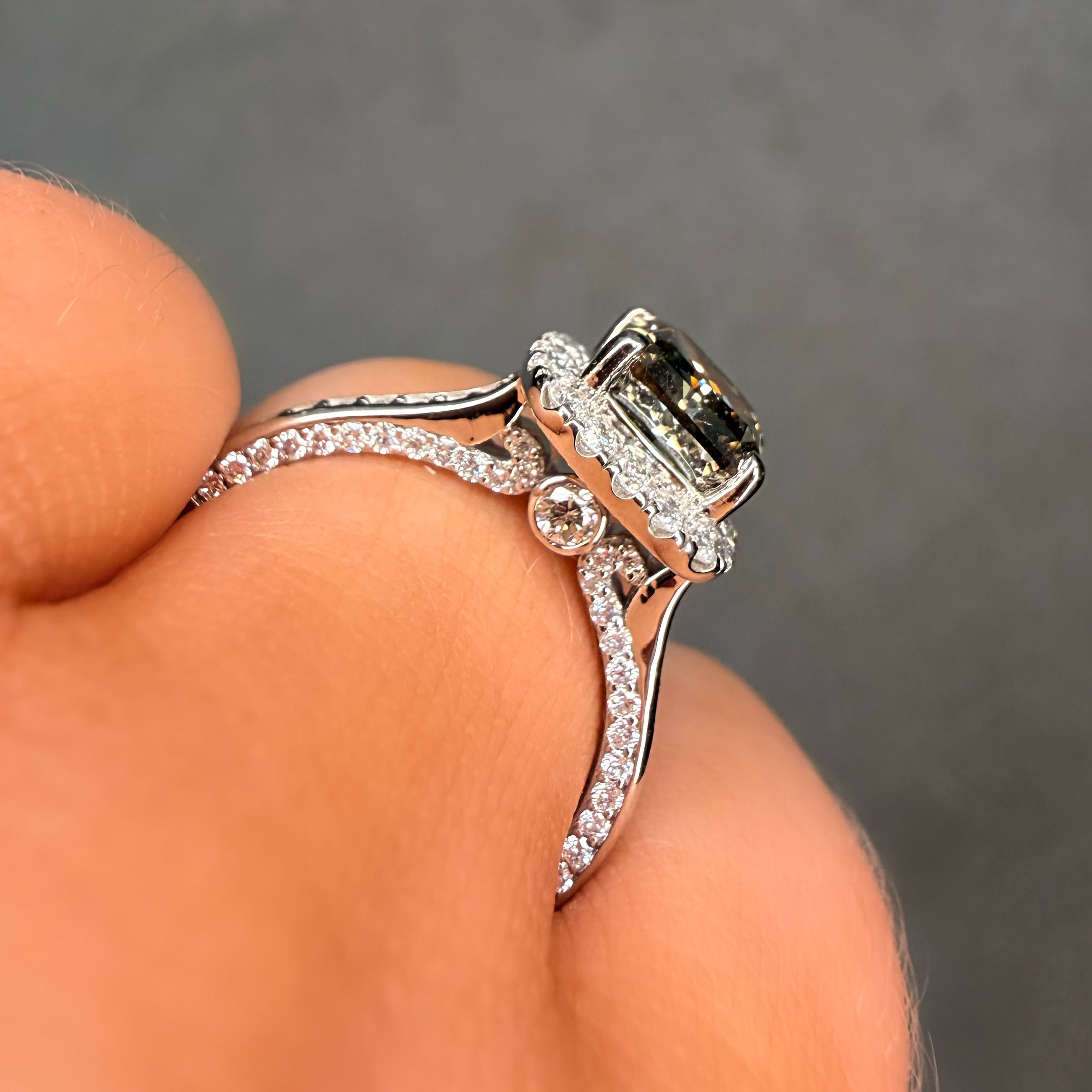 Close-up of a silver ring with a central gemstone held between fingers against a dark background