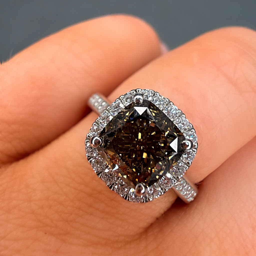 Diamond ring with a dark stone held on a finger against a neutral background
