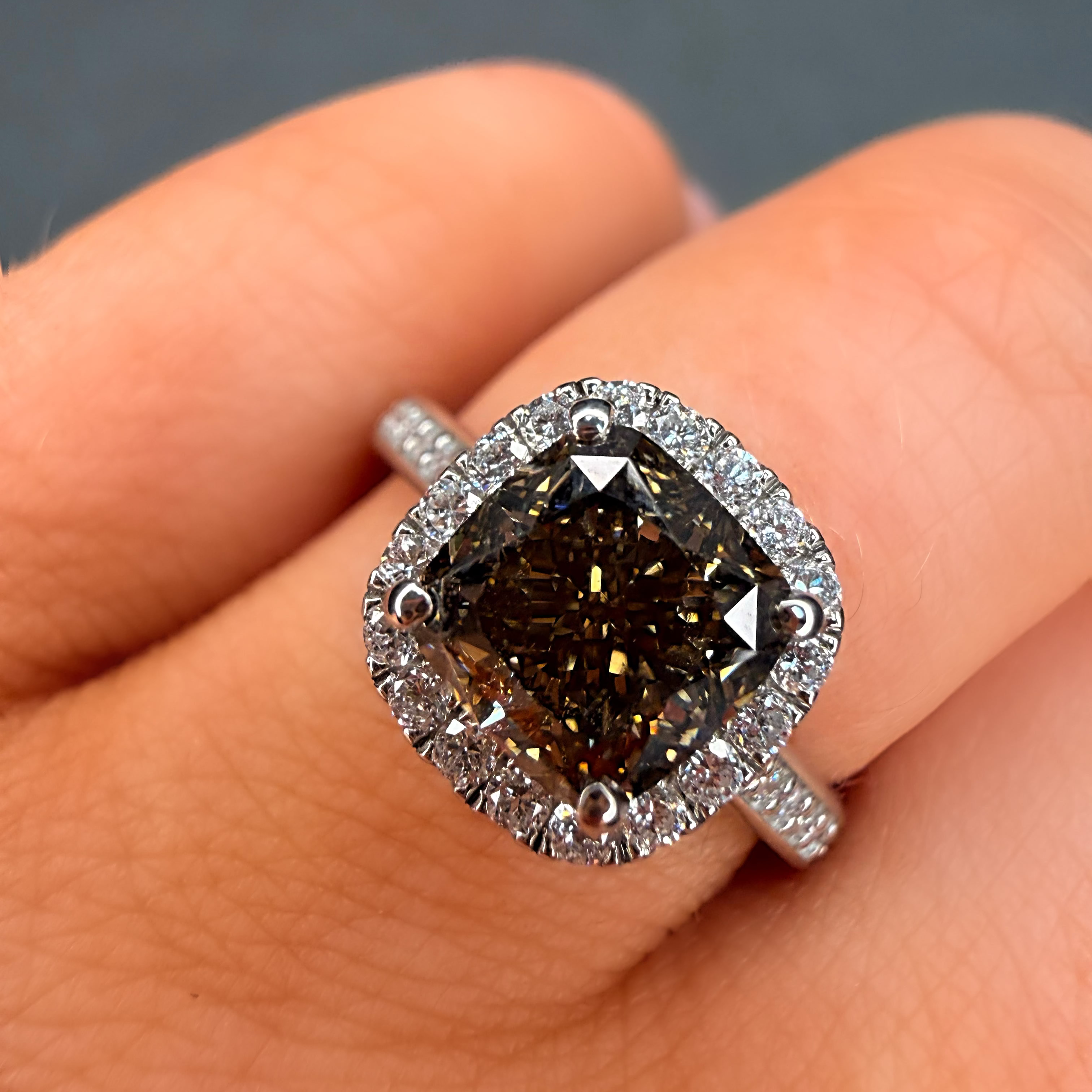 Diamond ring with a dark stone held on a finger against a neutral background