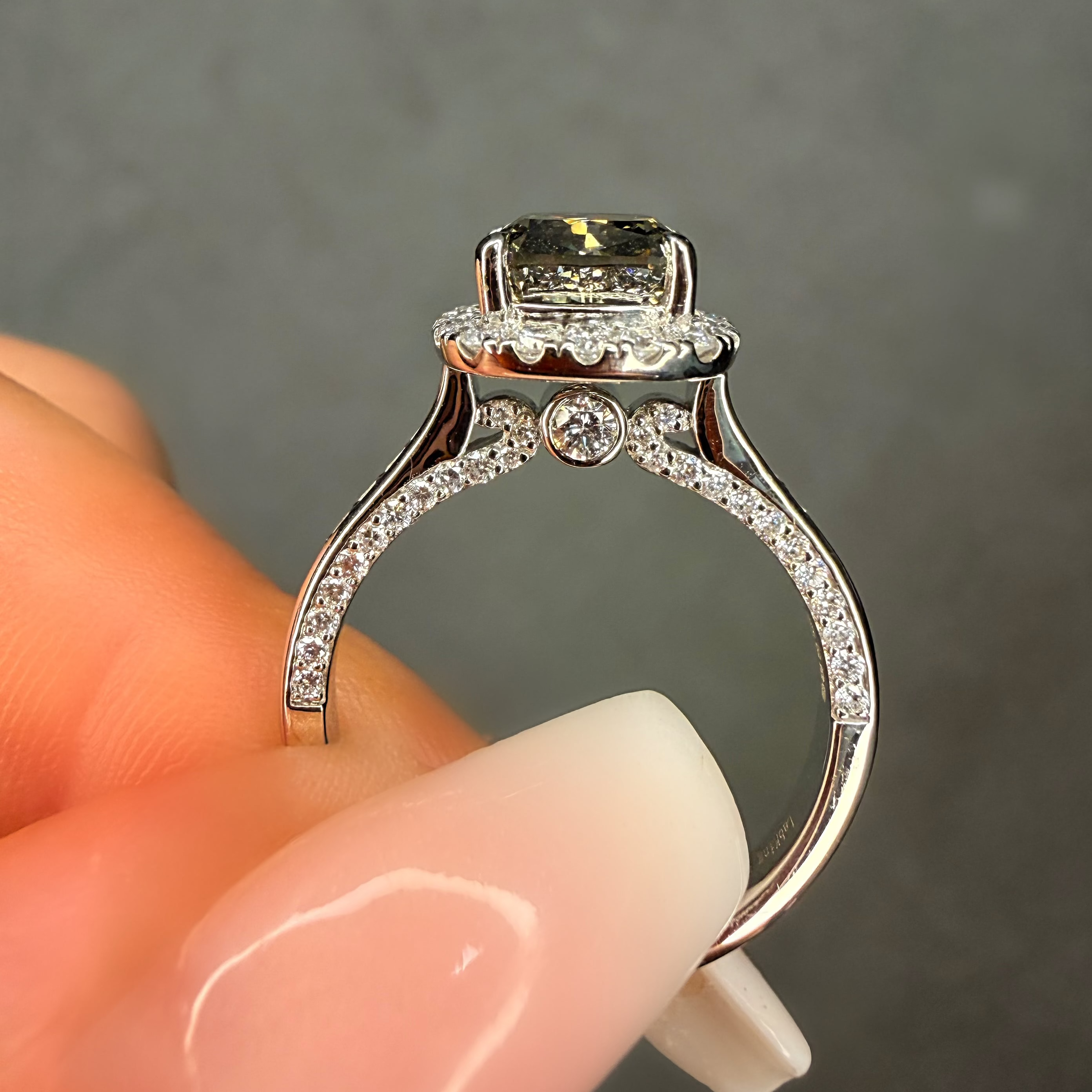 Silver ring with a large central stone held by a hand against a gray background